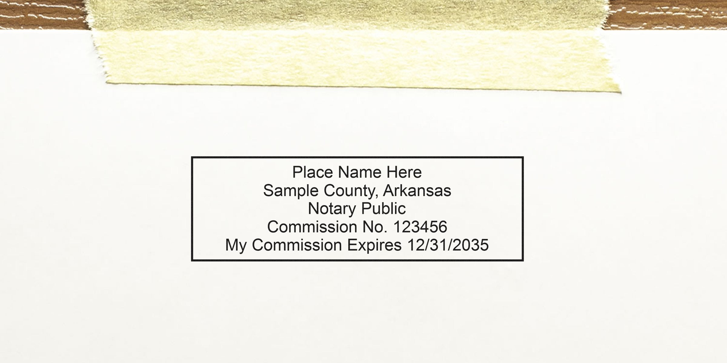 Rectangular notary stamp mockup on white paper with masking tape at top reading "Place Name Here, Sample County, Arkansas, Notary Public, Commission No. 123456, My Commission Expires 12/31/2035"