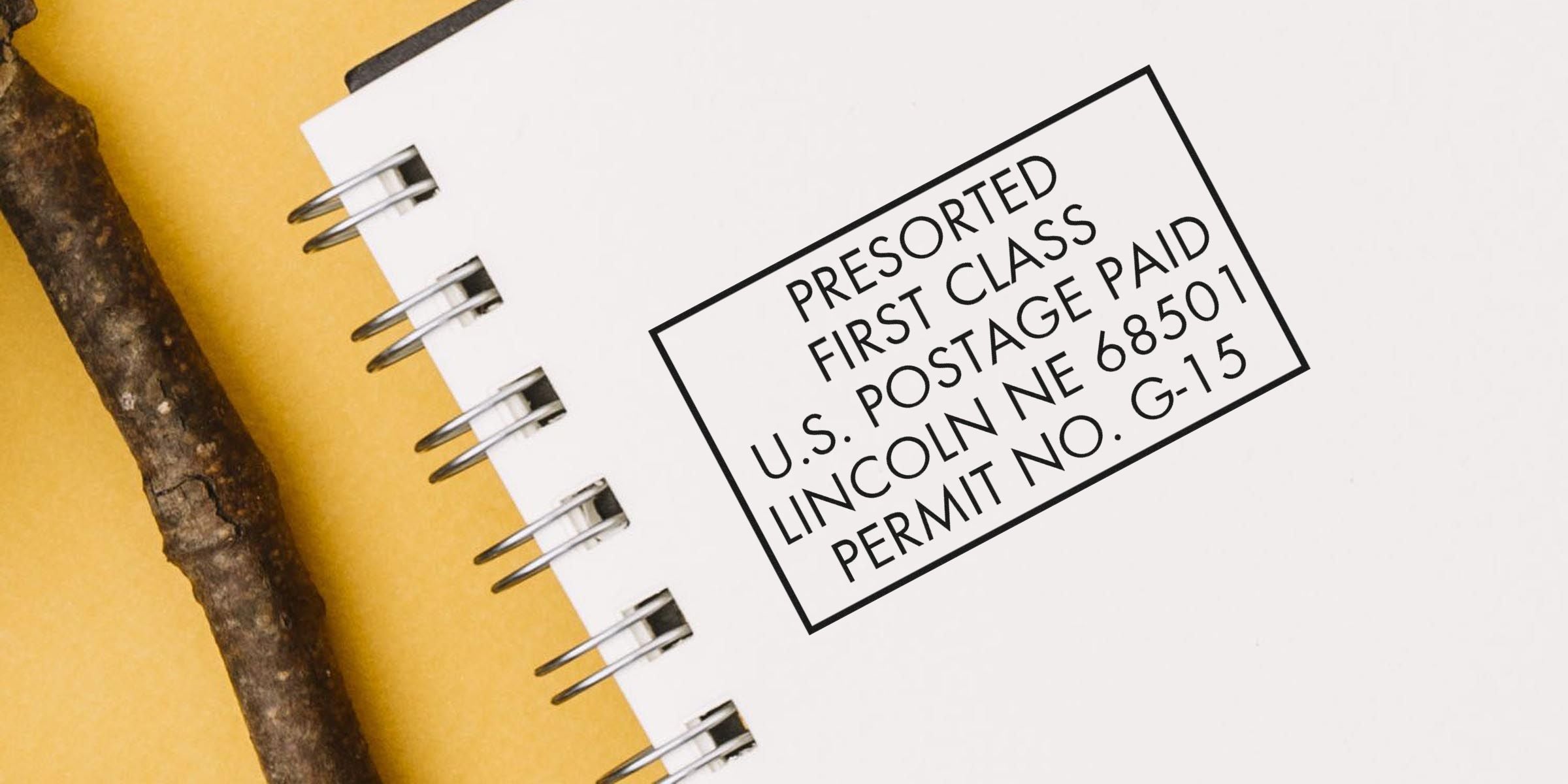 Label on a white notebook page: “PRESORTED FIRST CLASS U.S. POSTAGE PAID LINCOLN NE 68501 PERMIT NO. G-15” with a brown twig beside it.