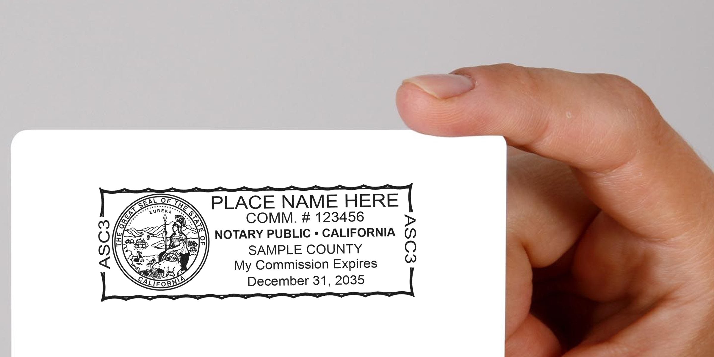 Hand holding white card showing California notary public seal and sample text "PLACE NAME HERE", commission number, sample county and commission expiration date, black stamped border and ASC3 markings.