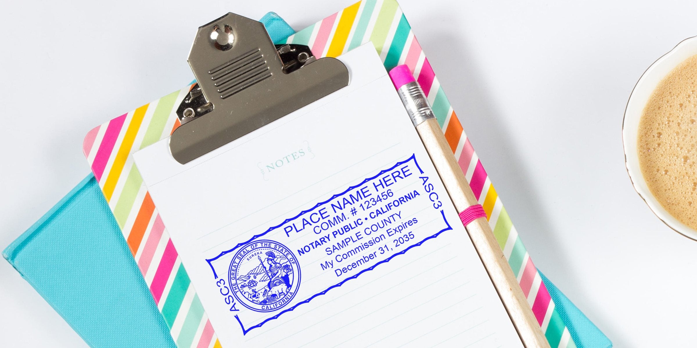 Top-down view of clipboard with colorful striped cover, lined notepad showing blue California notary public stamp/sample, wooden pencil with pink eraser and cup of coffee.