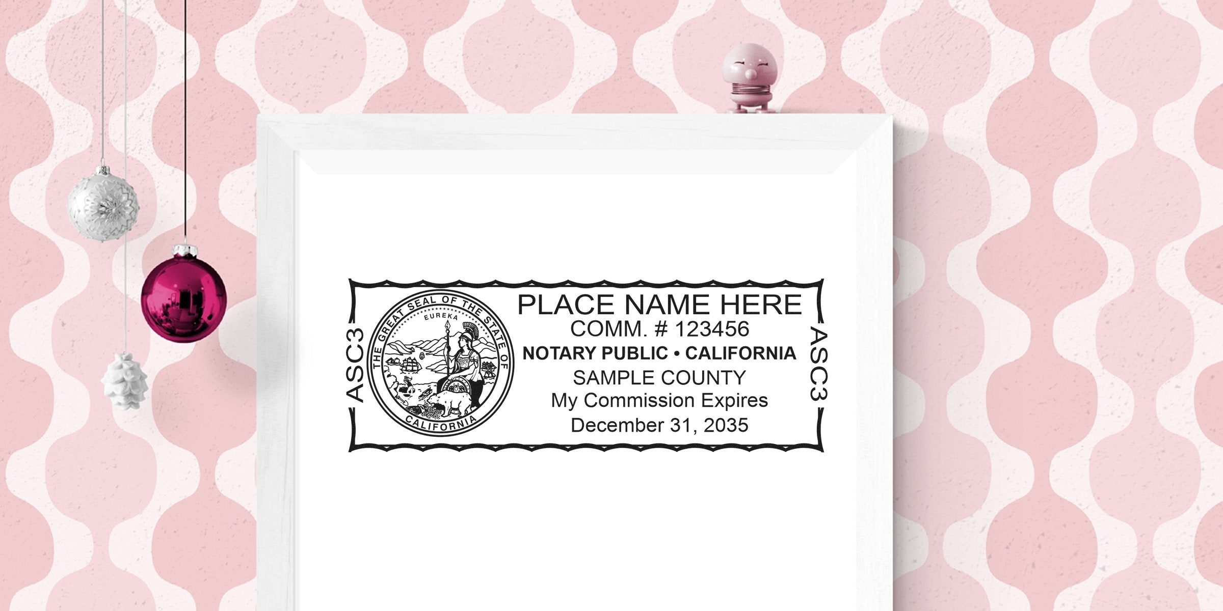 Framed mockup of a California notary stamp with seal and sample text on white paper, displayed against pink patterned wallpaper with hanging holiday ornaments.