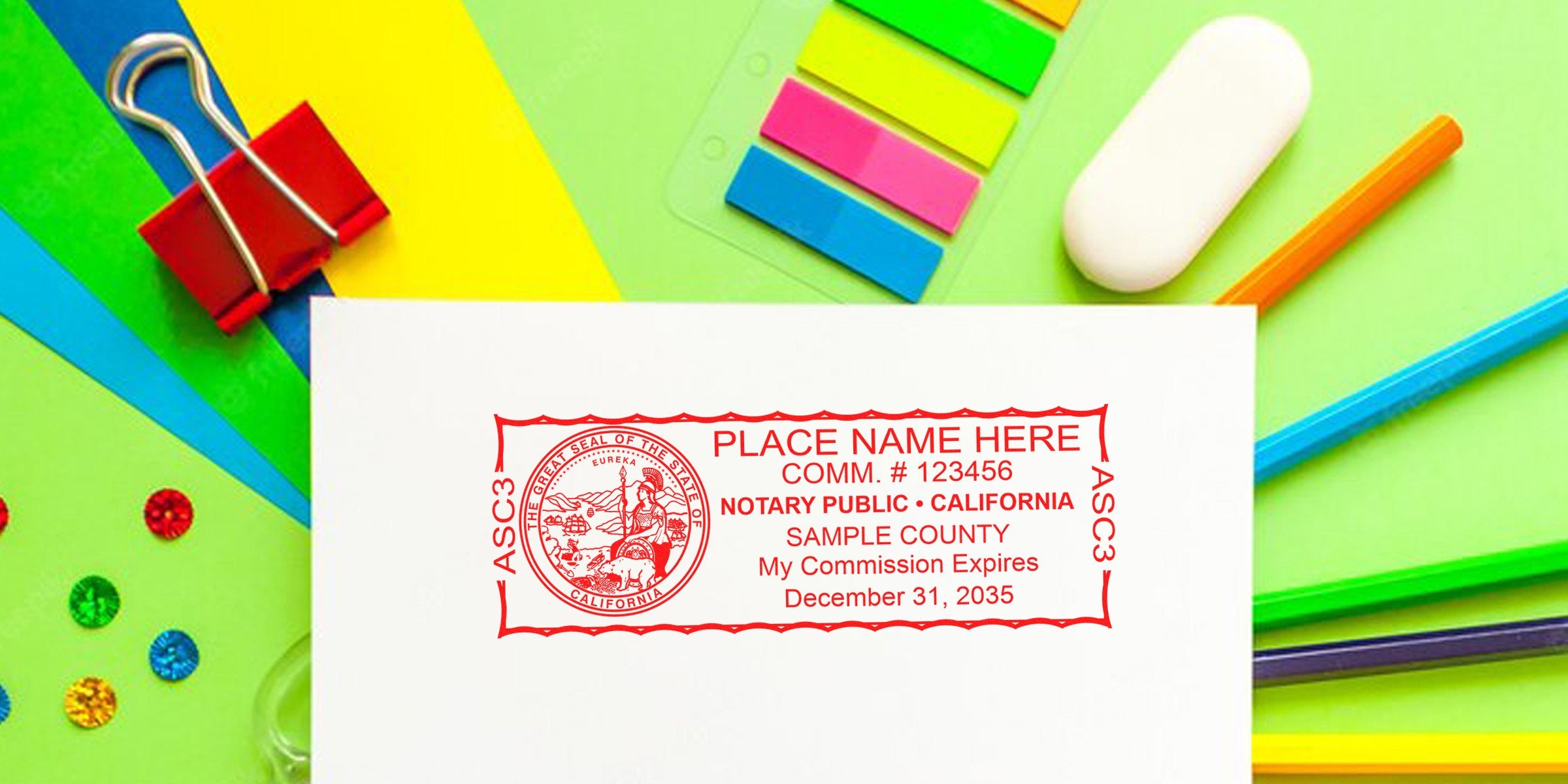 Red California notary public stamp sample on white paper surrounded by colorful school supplies (pencils, binder clip, sticky tabs, eraser) on green background — customizable name, commission number, expiration date