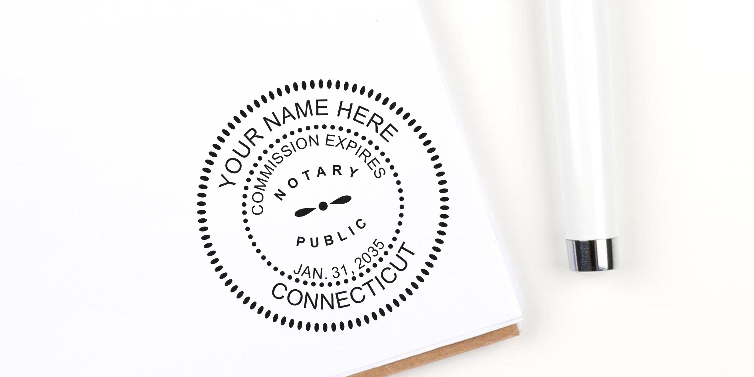 Round black notary public stamp on white paper reading "Your Name Here, Connecticut, Jan. 31, 2035" with nearby white pen — customizable notary seal image