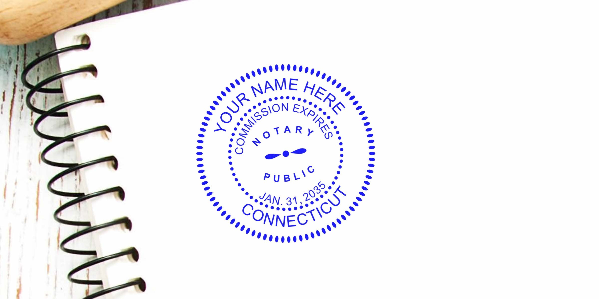 Blue circular notary public stamp reading "Connecticut" and "Notary Public" on white paper beside a black spiral notebook and wooden handle