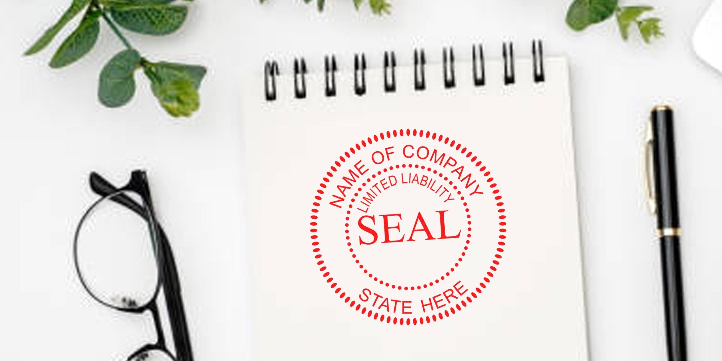 White desk scene with a spiral notebook displaying a red circular “SEAL” stamp and placeholder text, surrounded by glasses, a black pen, and green leaves.