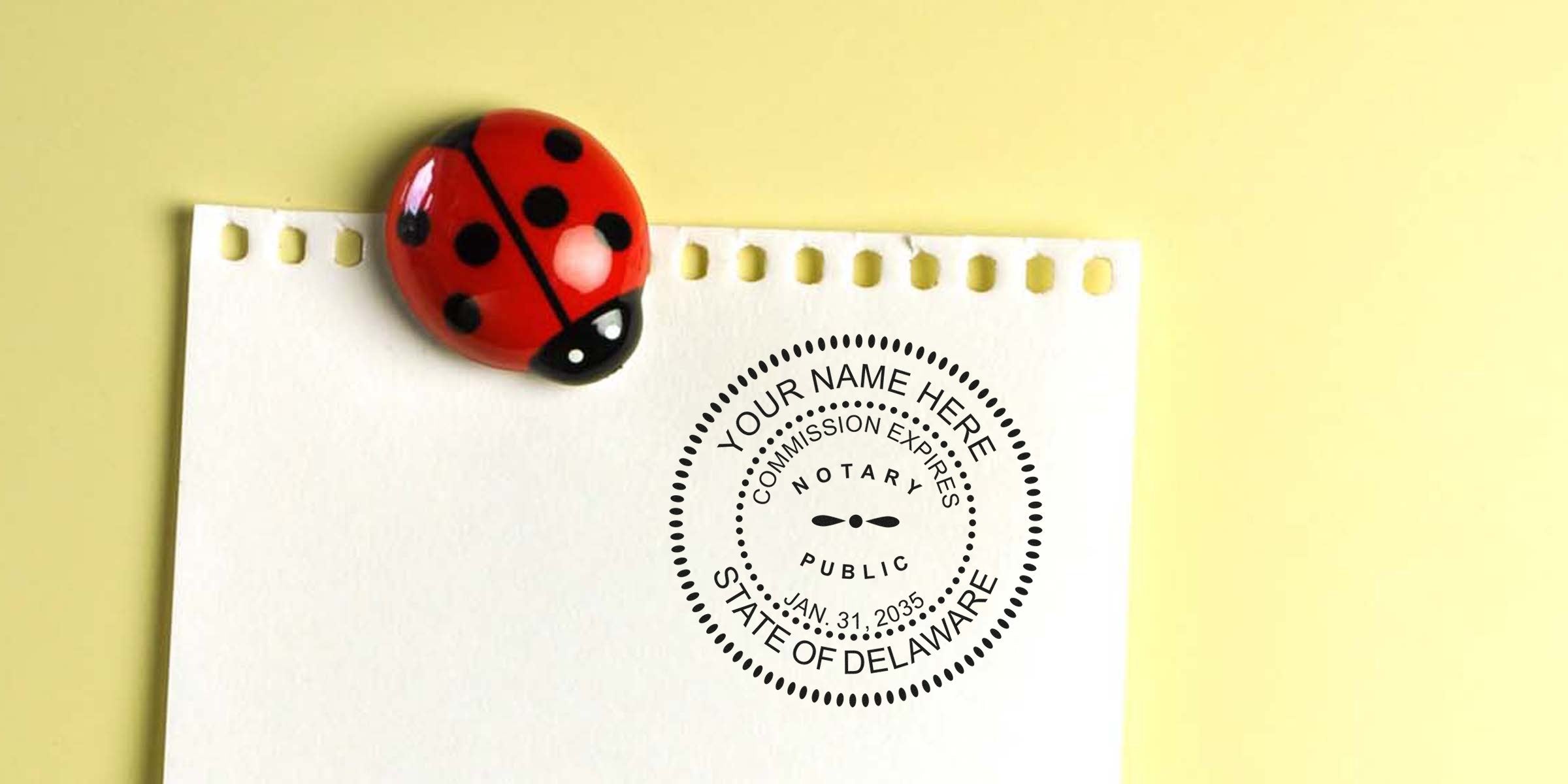 Top-down photo of torn white notebook paper pinned by a red ladybug magnet on a yellow background with a round State of Delaware notary public stamp printed on the paper