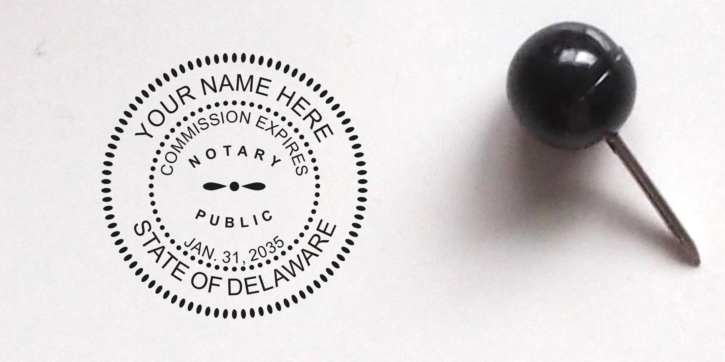 Black round notary public seal stamp reading "State of Delaware" and expiration date next to a black pushpin on white paper, close-up.