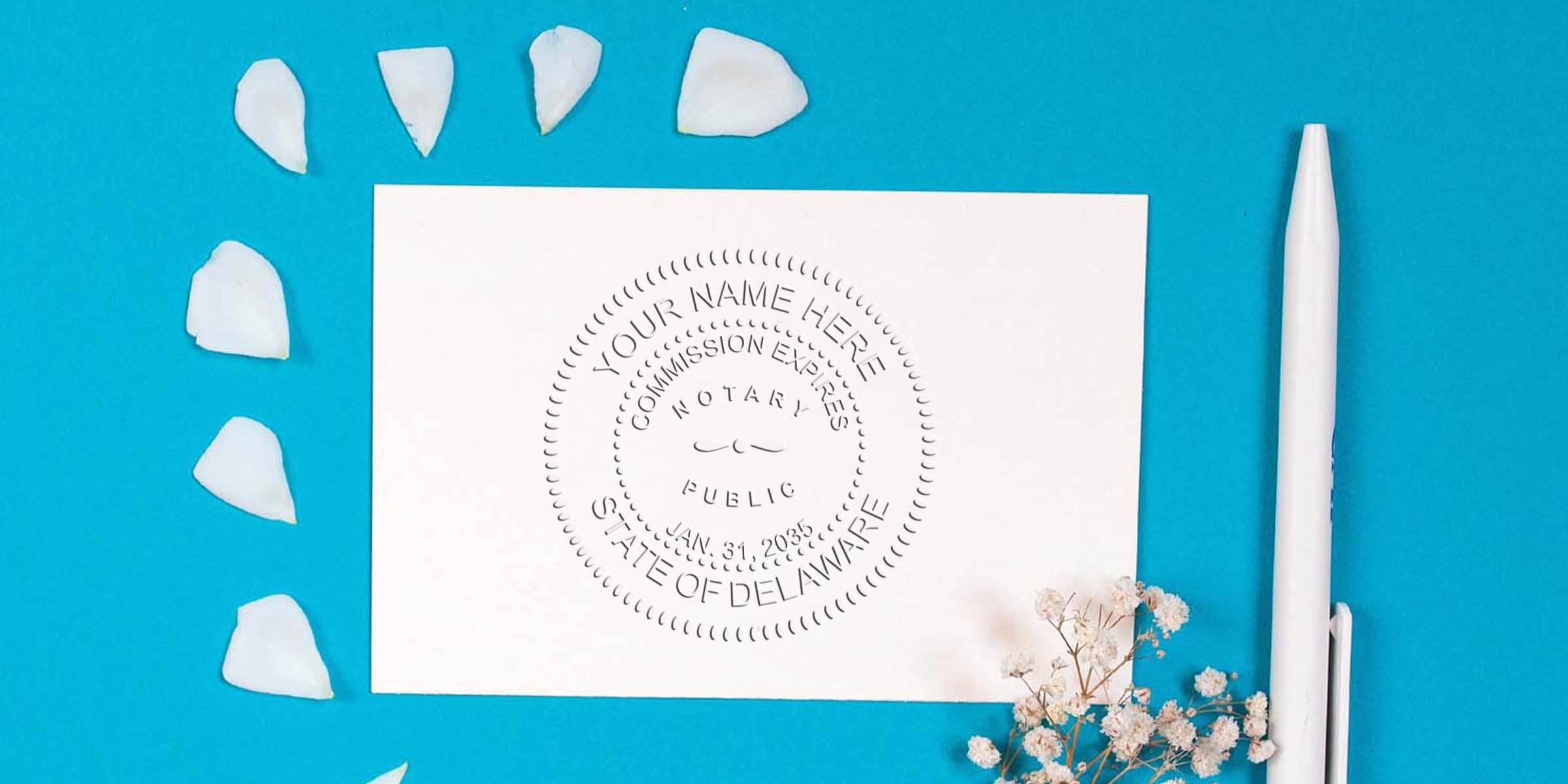 Embossed notary seal on white card reading "State of Delaware" on turquoise background with white pen, scattered white petals and baby’s breath flowers