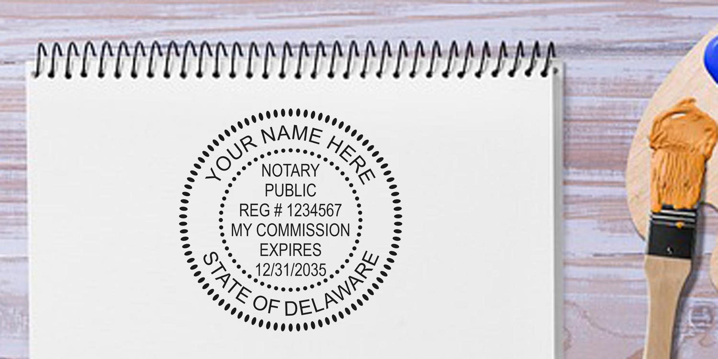 Mock notary public seal printed on a spiral notebook page reading "Your Name Here, Notary Public, Reg #1234567, My Commission Expires 12/31/2035, State of Delaware," with a paintbrush on a light wooden table background