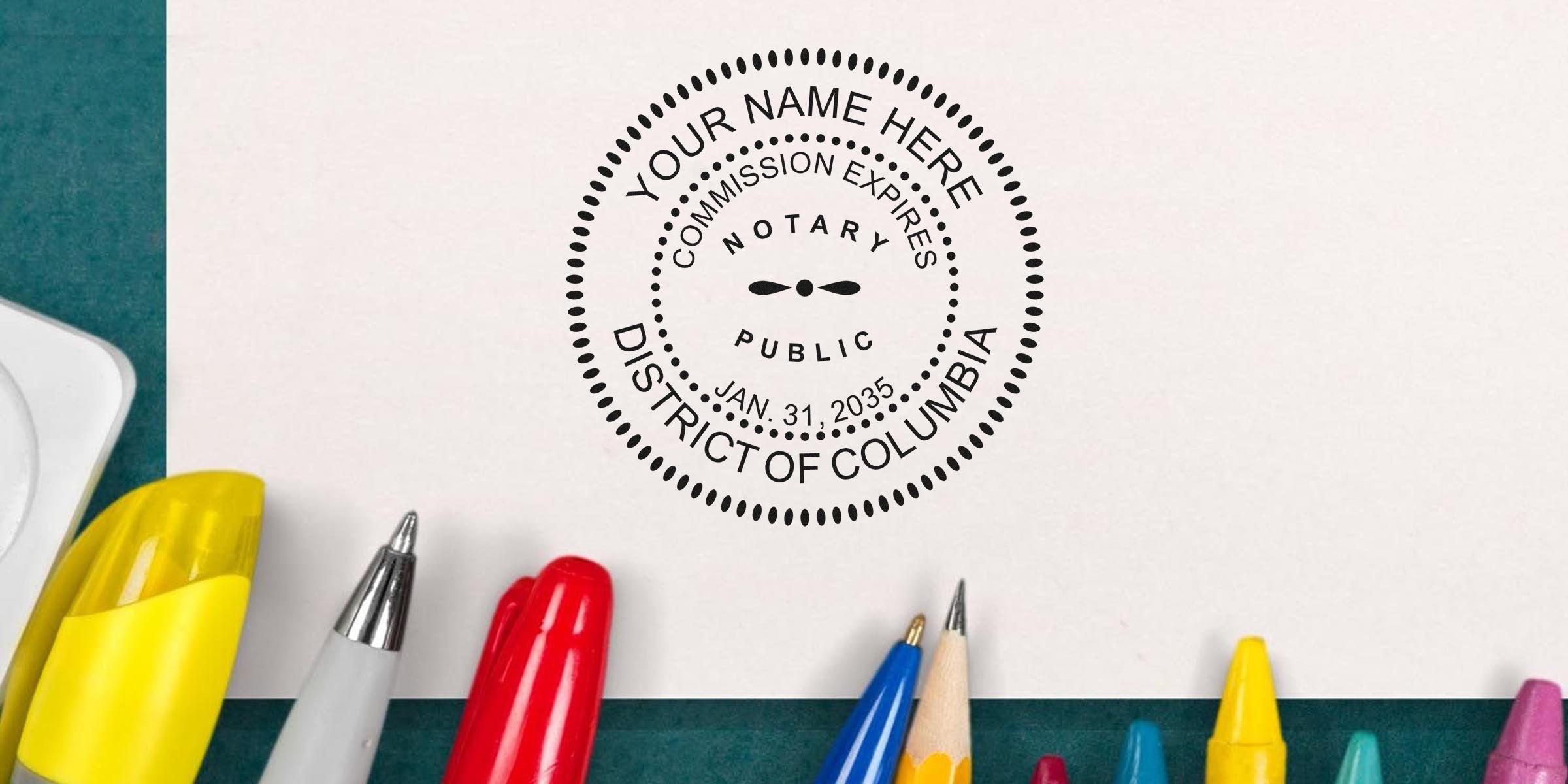 Notary public circular seal stamp reading "District of Columbia" on white paper, with colorful pens, pencils and crayons along the bottom — office stationery