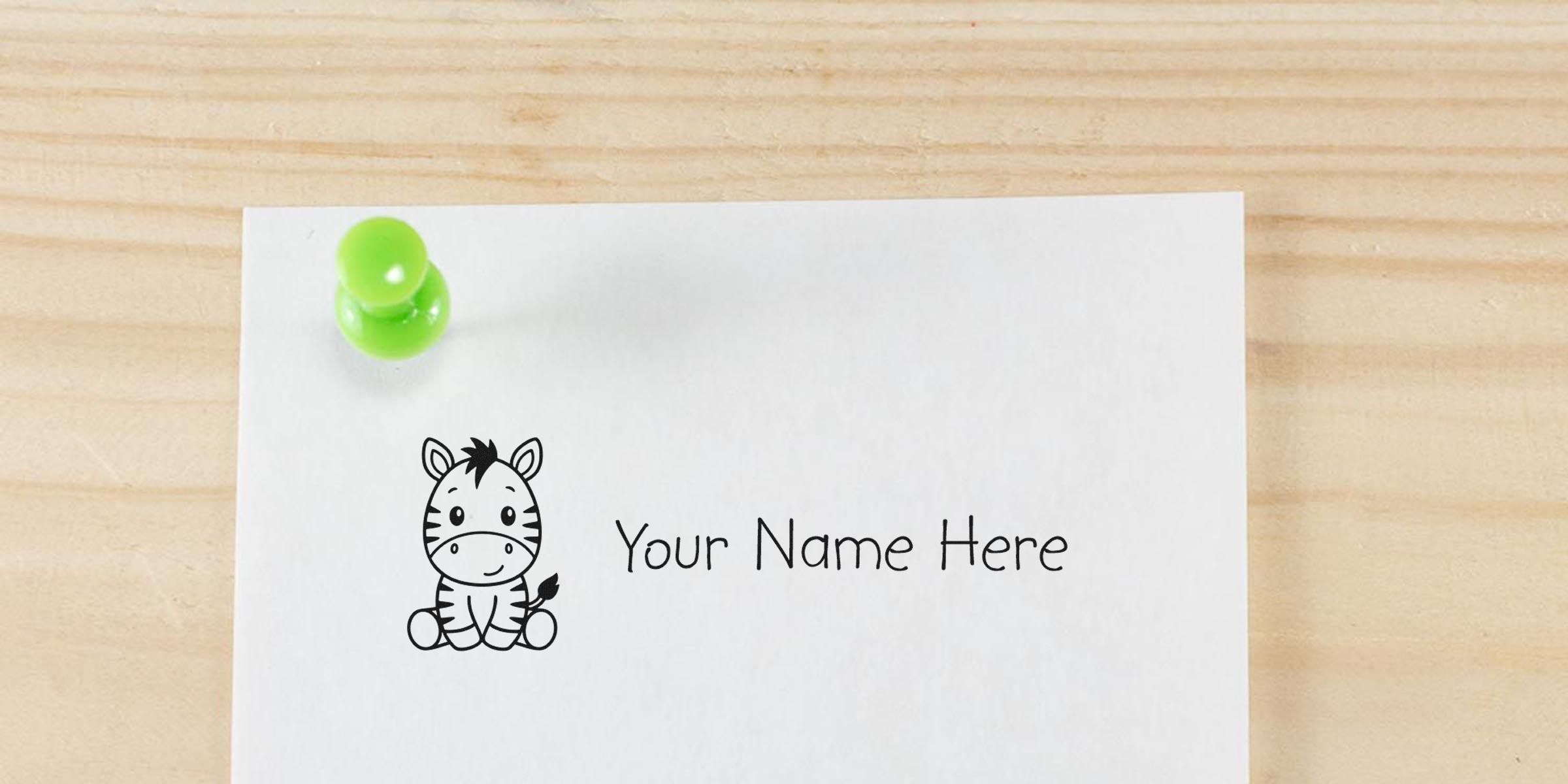 White card with a cute zebra illustration and the text “Your Name Here,” pinned by a green push pin on a wooden surface.