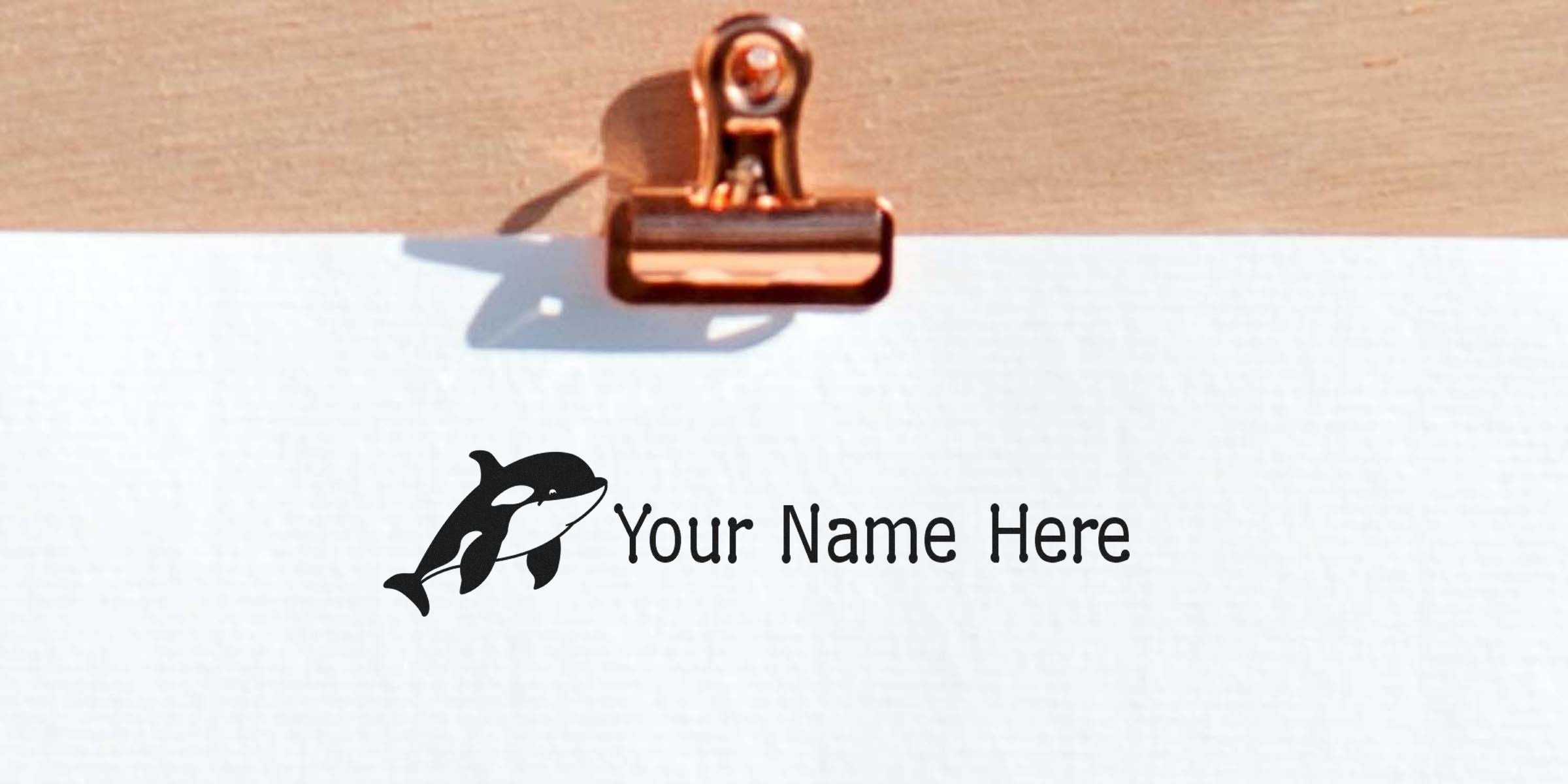 Dolphin logo with the text “Your Name Here” on a white card held by a copper-colored binder clip.