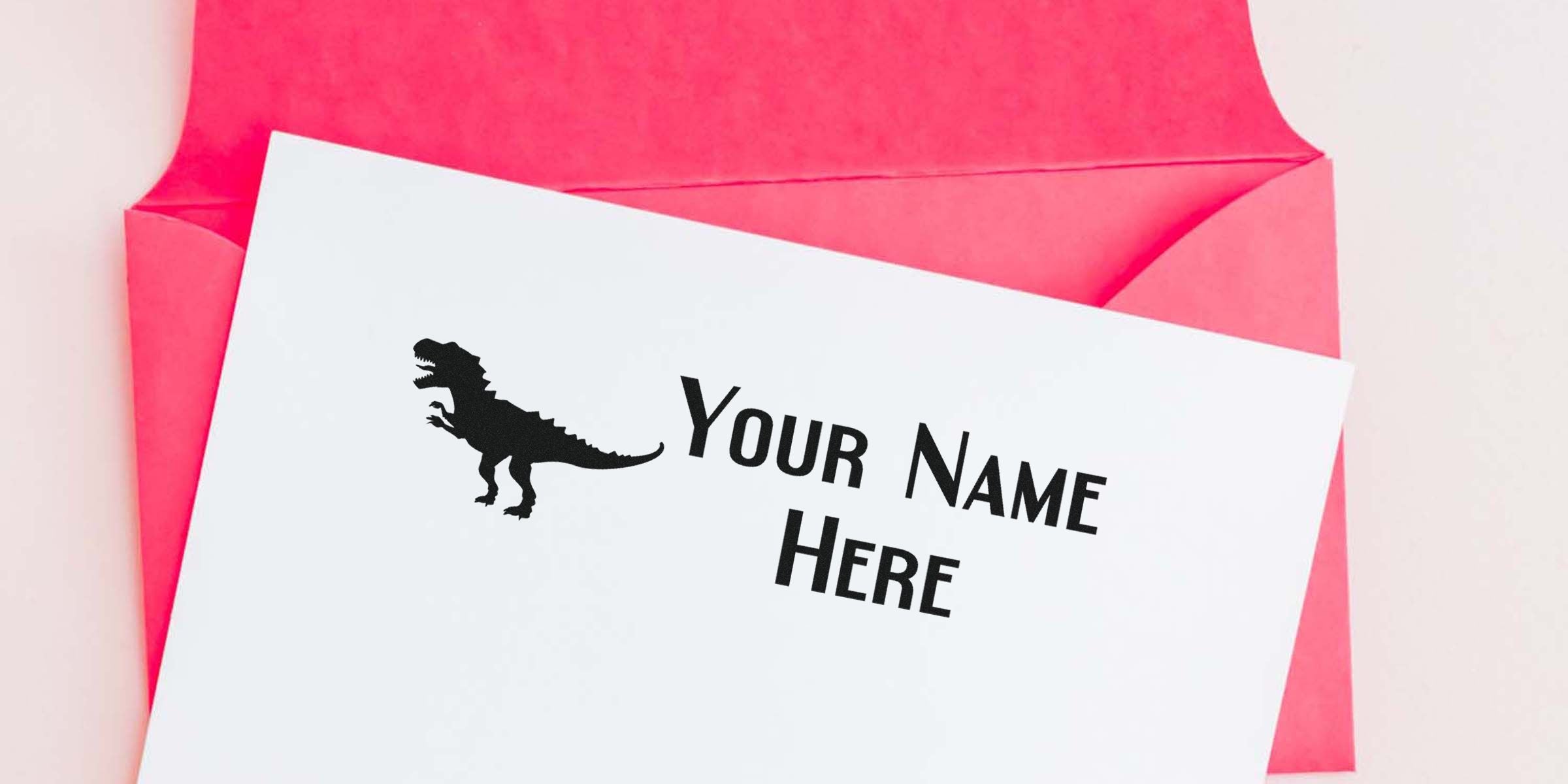 Card labeled "Your Name Here" with a black T-rex silhouette on white paper inside a pink envelope.