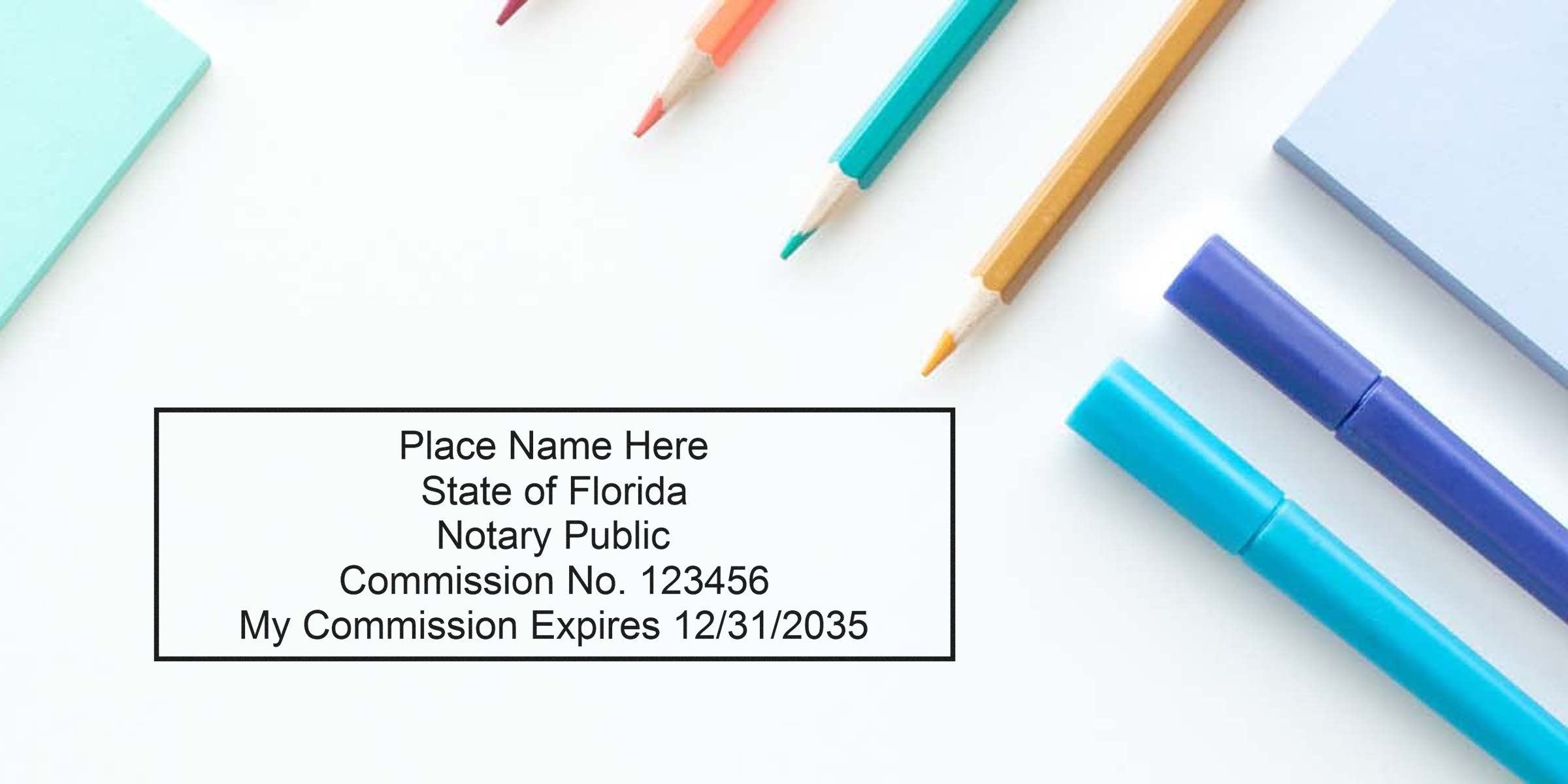 Flatlay of a customizable Florida notary public stamp sample showing commission number and expiration date inside a black rectangle, surrounded by colored pencils, blue markers and pastel sticky notes on a white background
