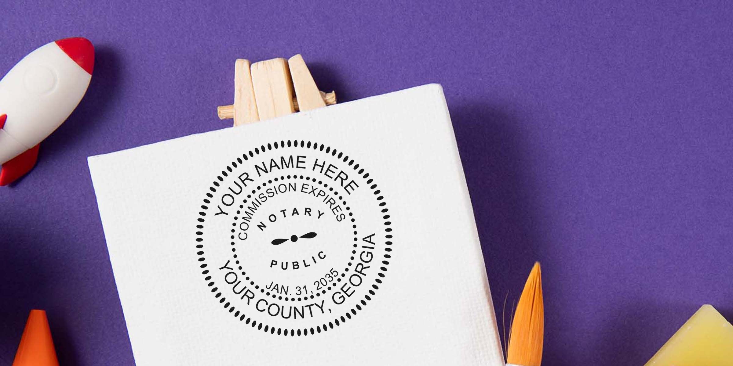 Notary public seal mockup on white canvas with custom stamp design, "Your Name Here" and county placeholder, purple background, toy rocket and orange paintbrush nearby