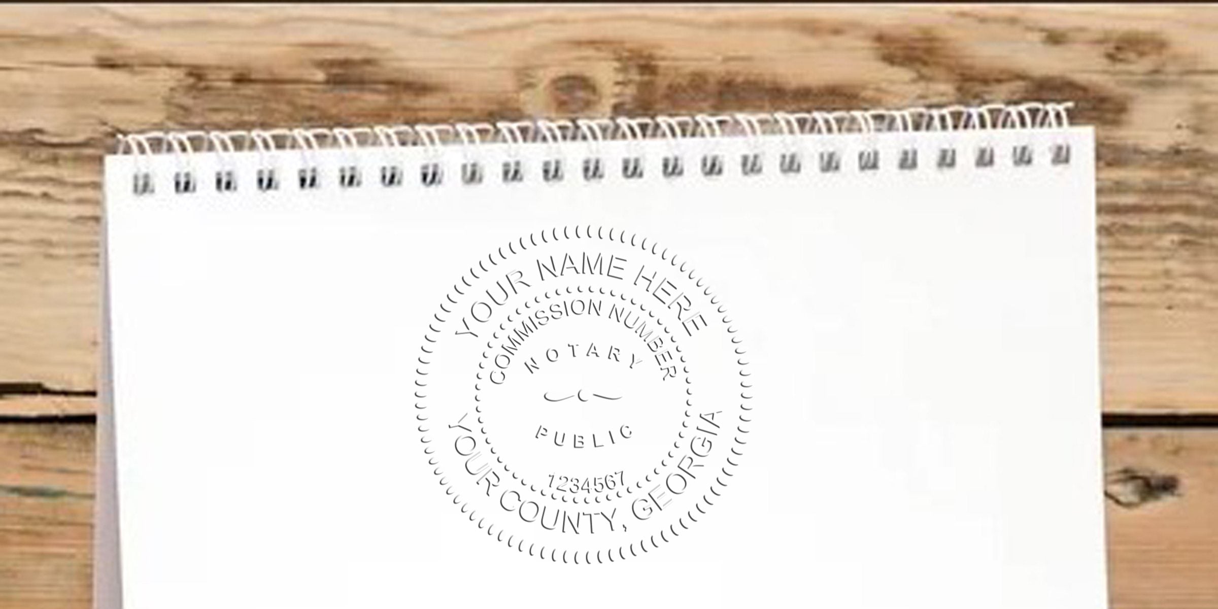 Top spiral notepad on wooden table with gray circular notary seal mockup reading "Your Name Here, Commission Number, Notary Public, Your County, Georgia"