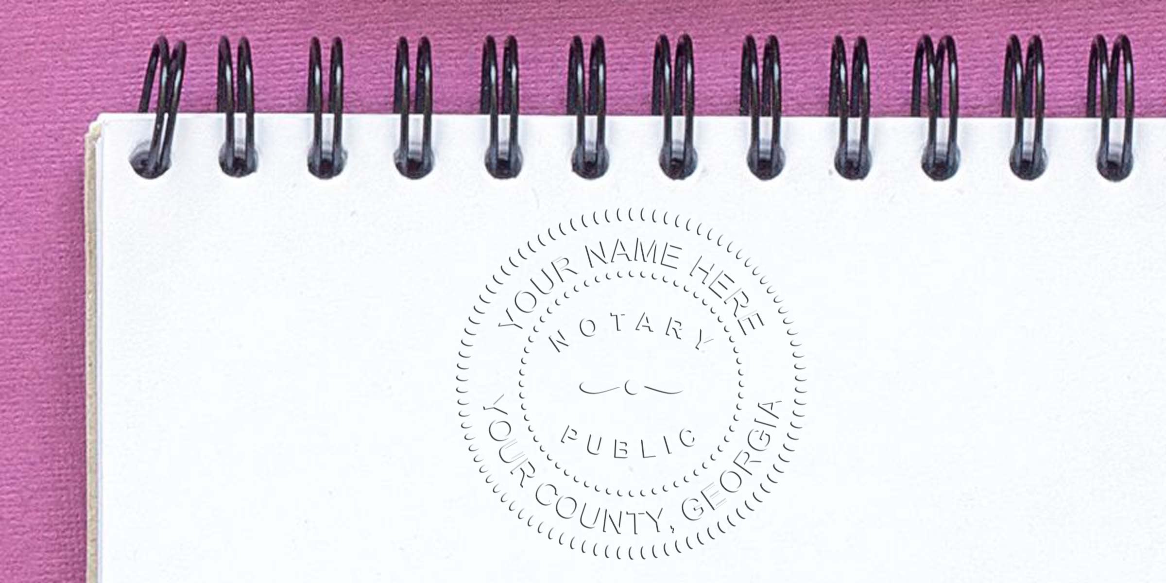 Spiral-bound white notebook on pink background with an embossed circular notary public seal reading "Your Name Here, Your County, Georgia" centered on the page — notary seal, embossed impression, stationery photo
