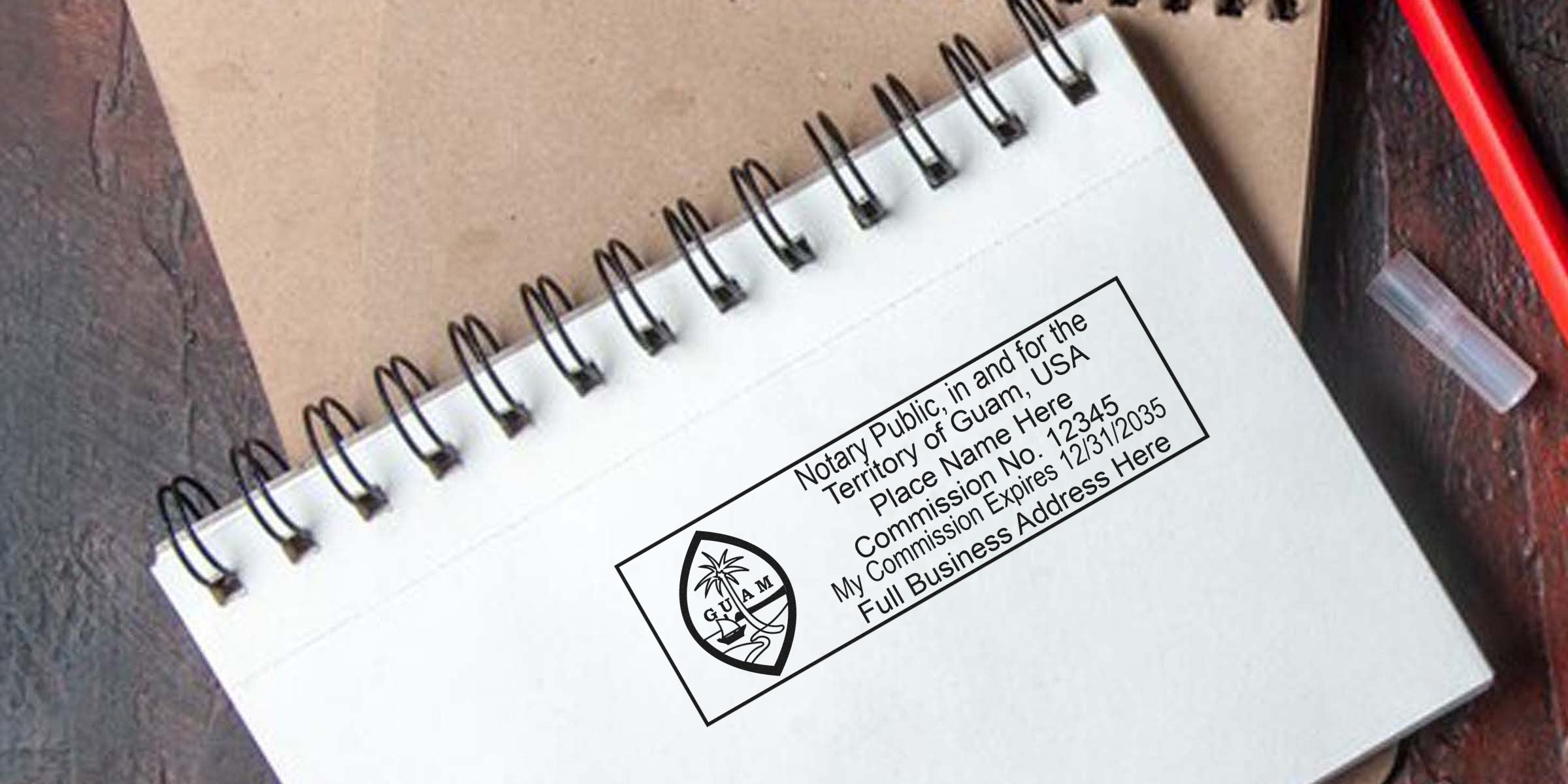 Spiral-bound notebook page stamped with rectangular Guam notary public seal and commission details in black ink, with a red pen cap and kraft notebook in background