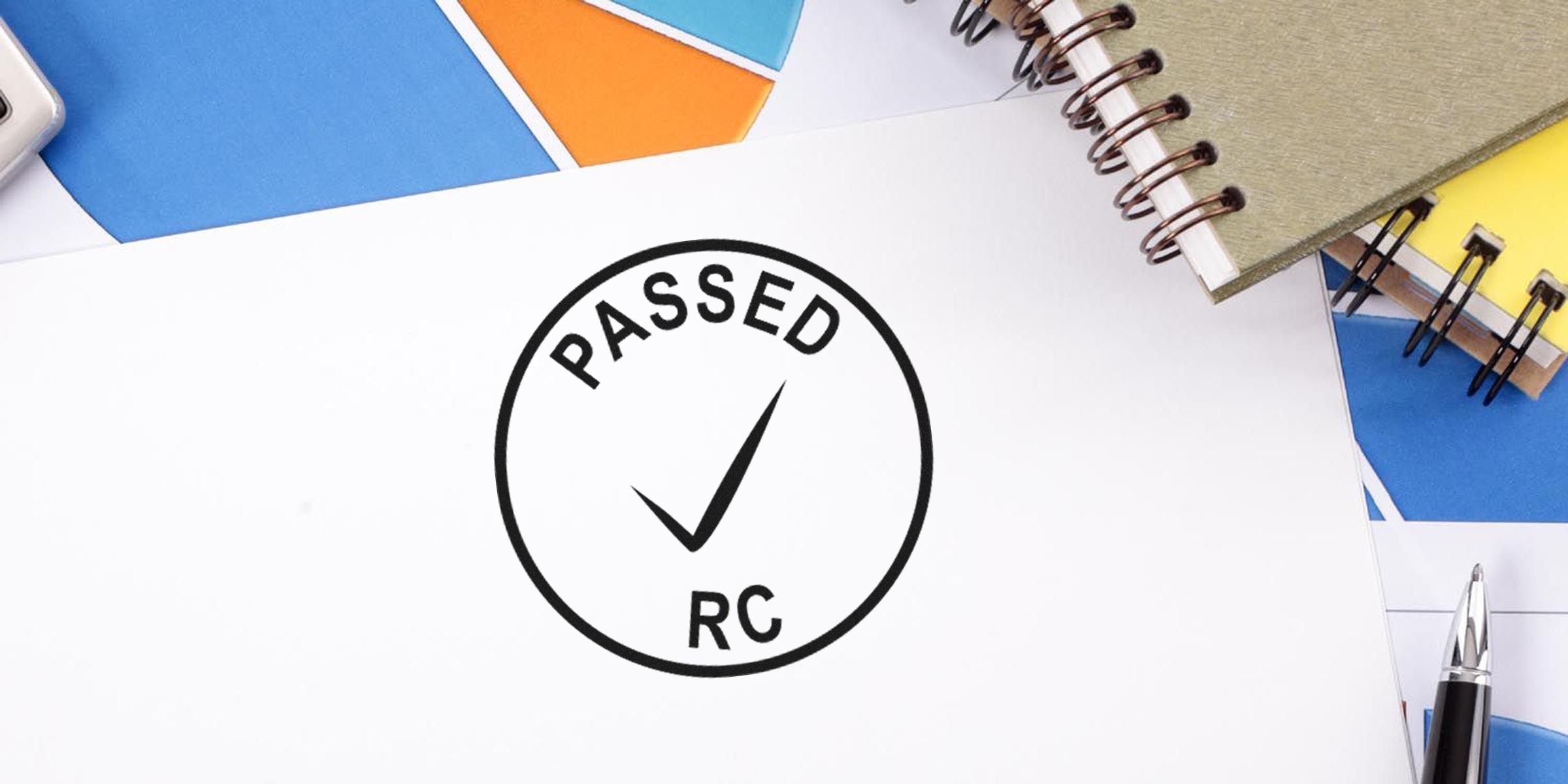 Circular stamp with the word 'PASSED RC' and a checkmark on a desk with notebooks.