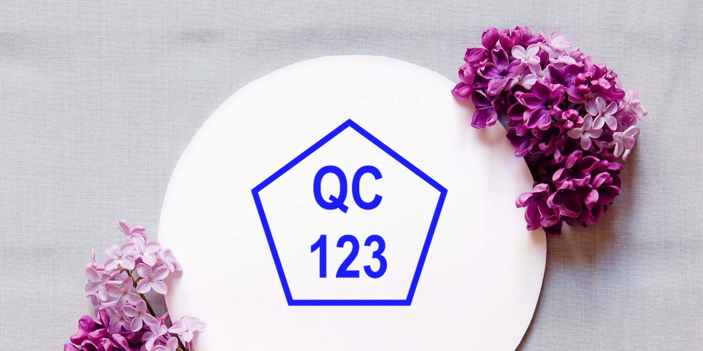 Plate with a blue pentagon outline reading “QC 123” on a white surface, bordered by pink and purple flowers.