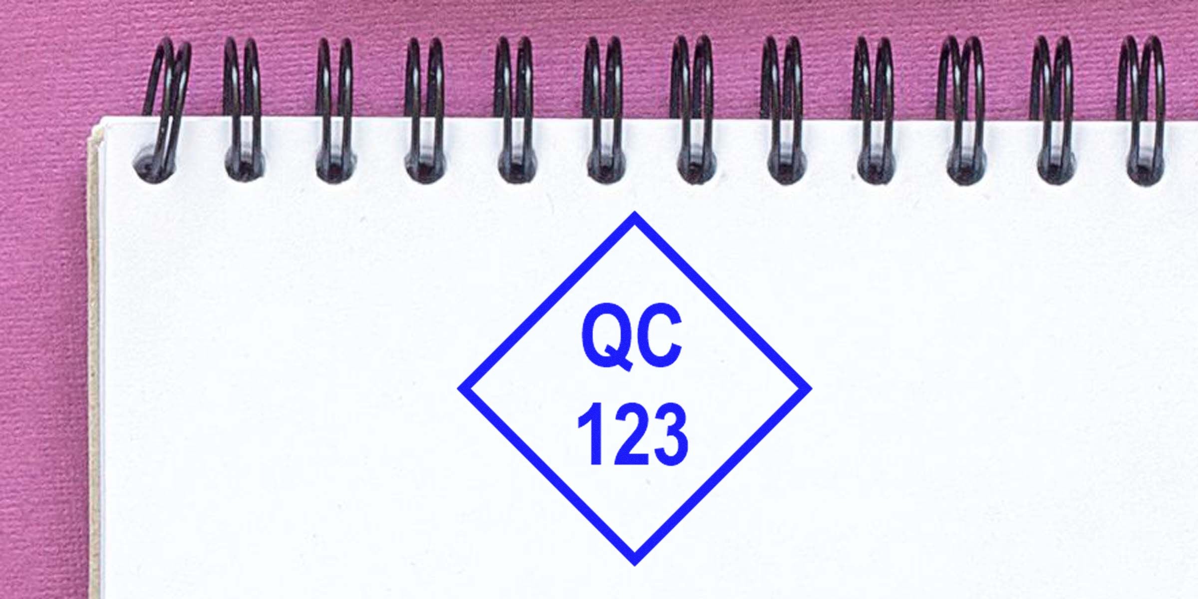 Diamond-shaped blue label with "QC 123" on a white notebook page.