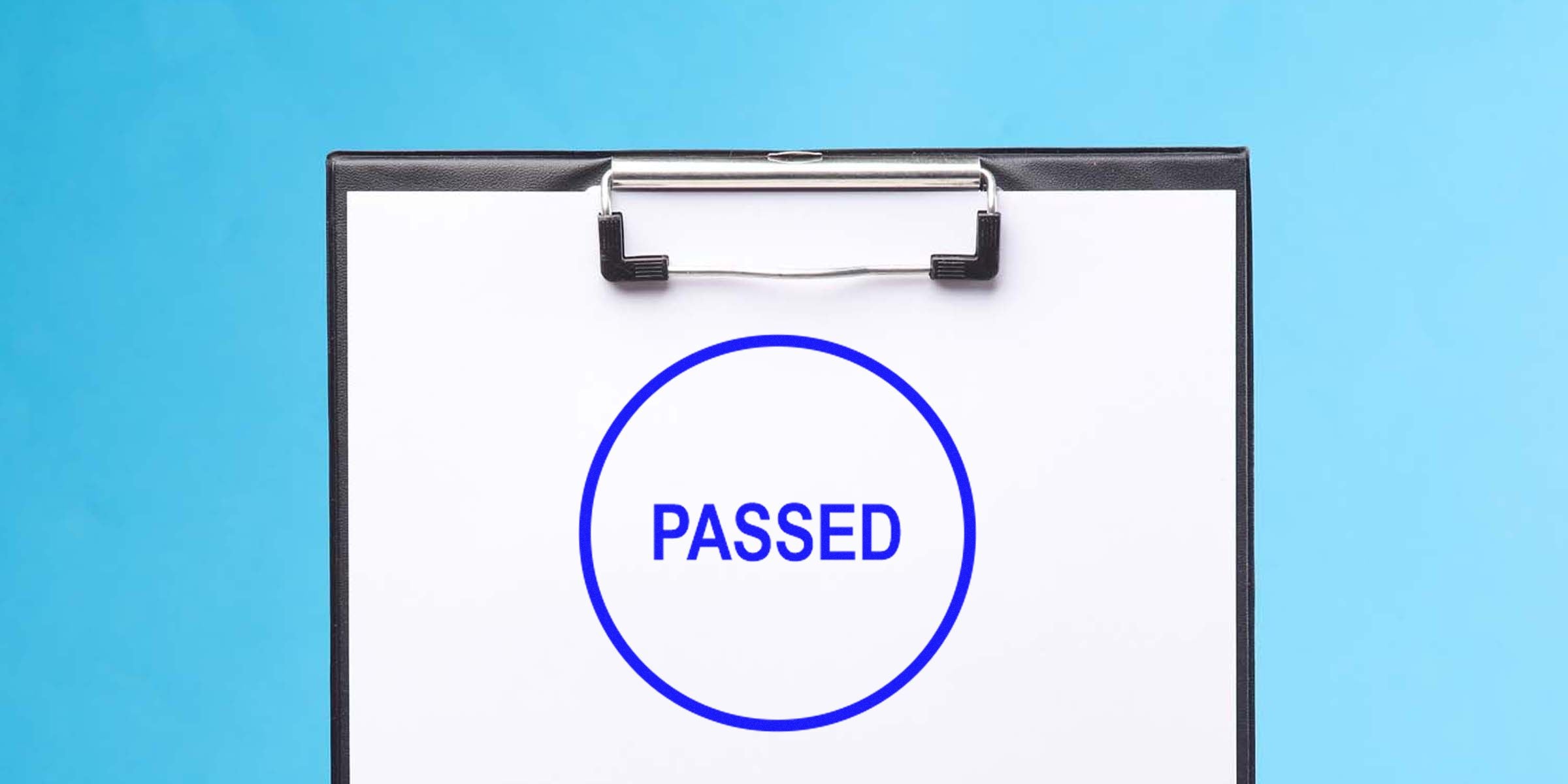 Clipboard with a white sheet showing a blue-outlined circle containing the word “PASSED.”