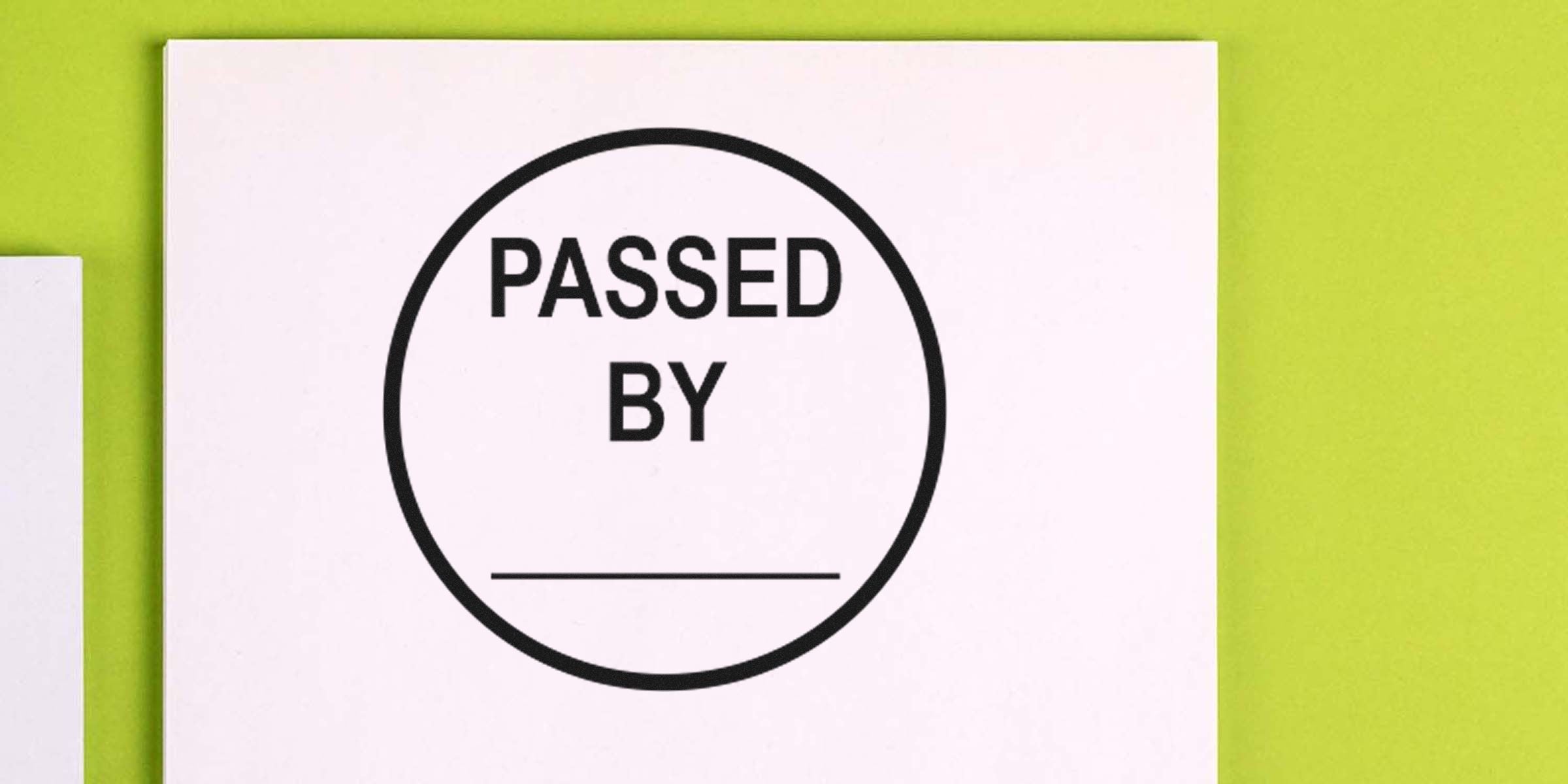 A white card with a black circular stamp reading “PASSED BY” and a short horizontal line underneath, set on a lime-green background.