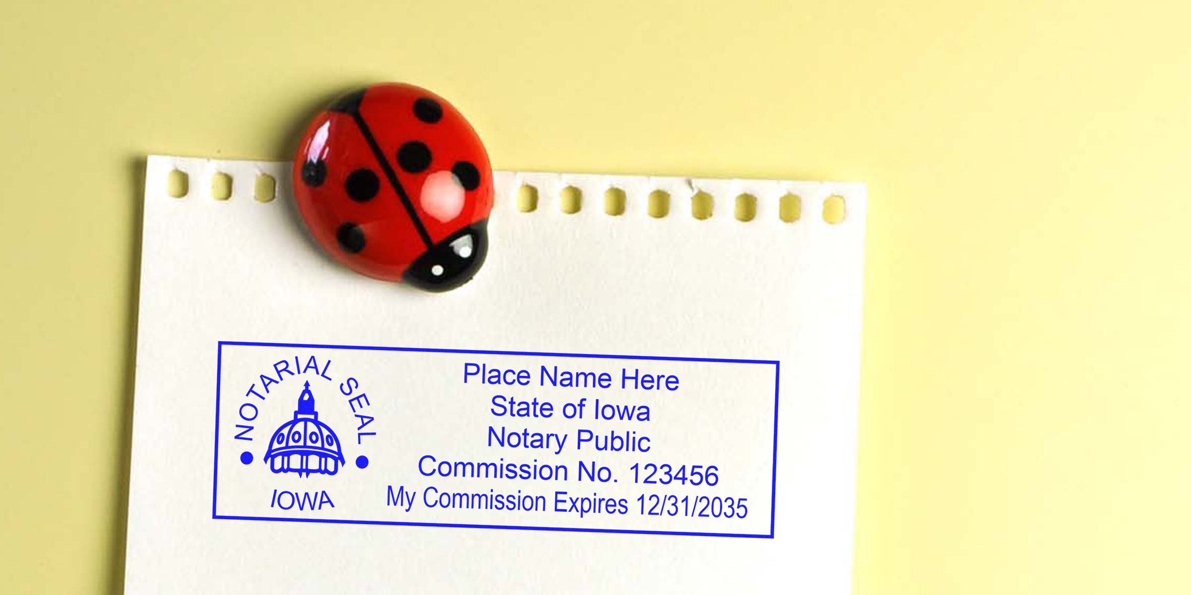 Blue Iowa notary public rubber stamp impression on white torn-edge paper, held by a red ladybug magnet against a pale yellow background