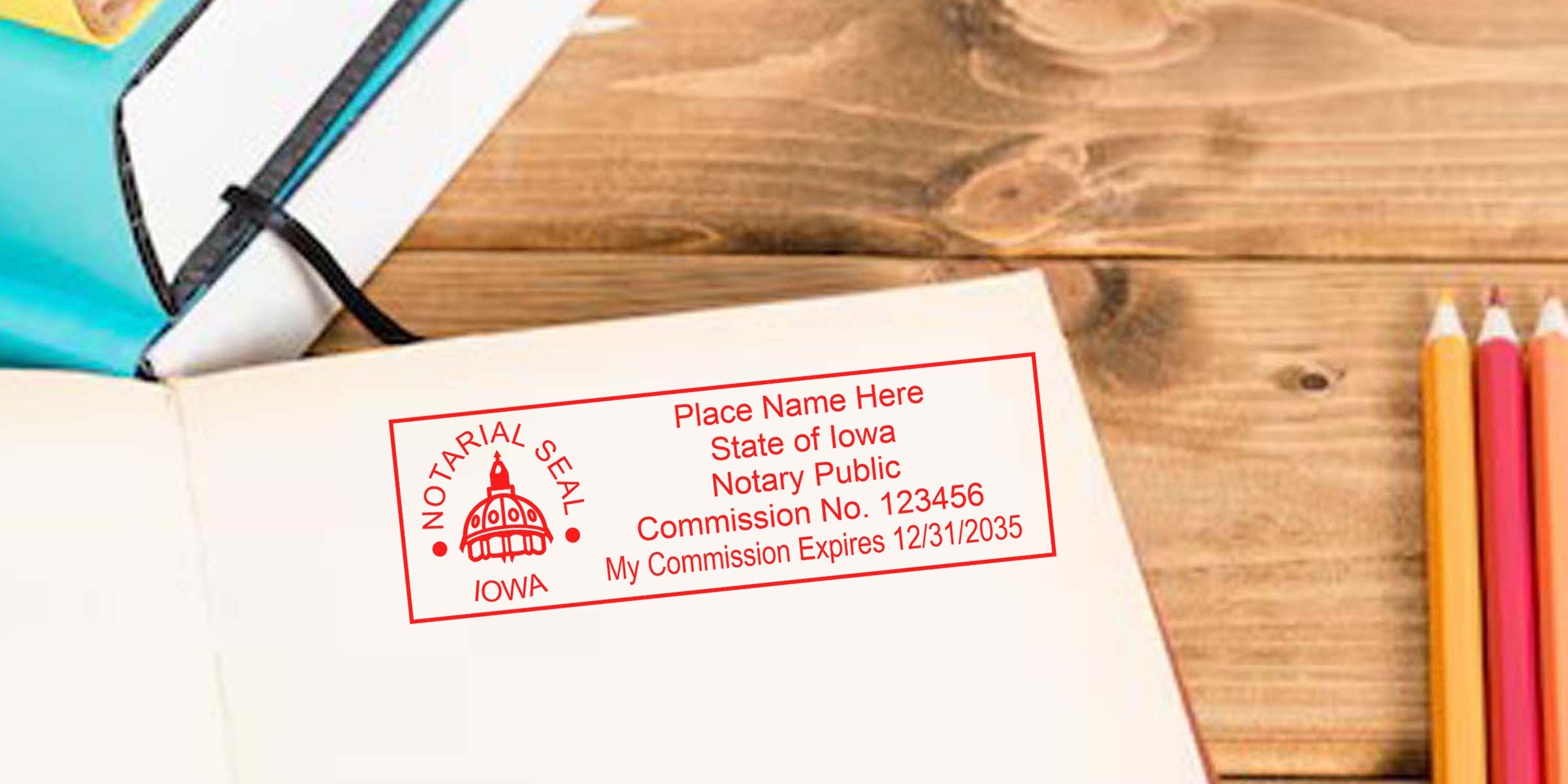 Red Iowa notary public seal stamped on an open notebook page on a wooden desk, with colored pencils and a teal notebook nearby, close-up office stationery scene for notary, legal, and document imagery.