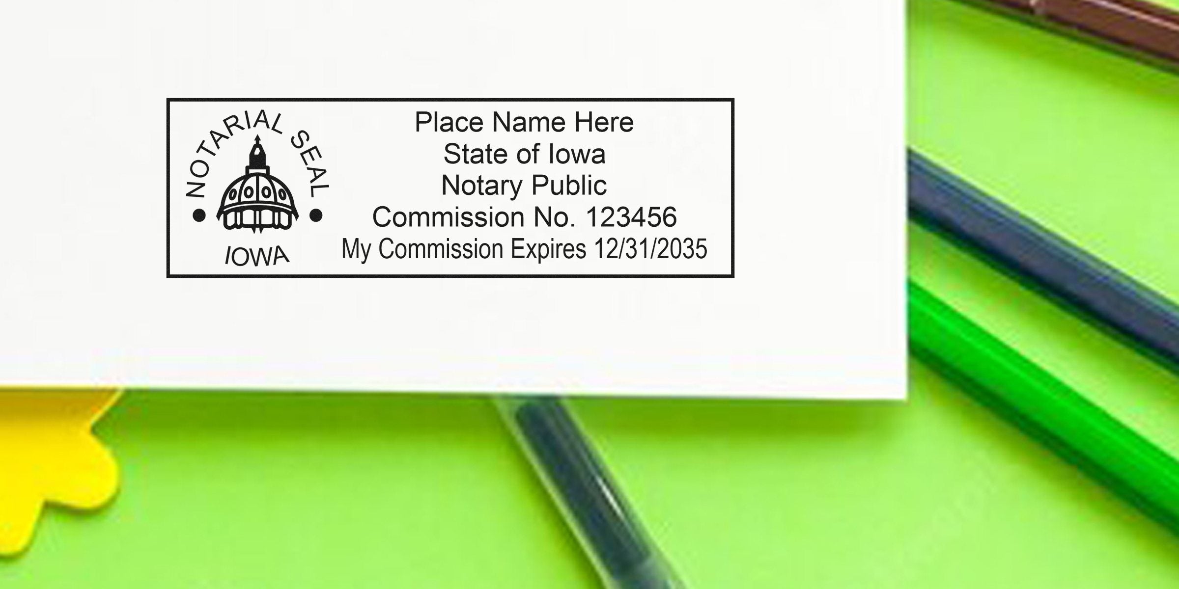 Rectangular Iowa notary seal sample on paper showing capitol dome logo, "Place Name Here", State of Iowa Notary Public, Commission No. 123456 and commission expiration date, on a green background with pens.
