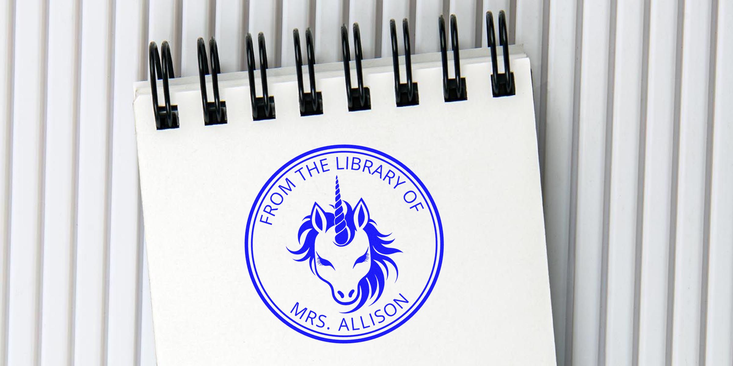 White spiral notebook page featuring a blue circular stamp with a unicorn and the text “From the Library of Mrs. Allison.”