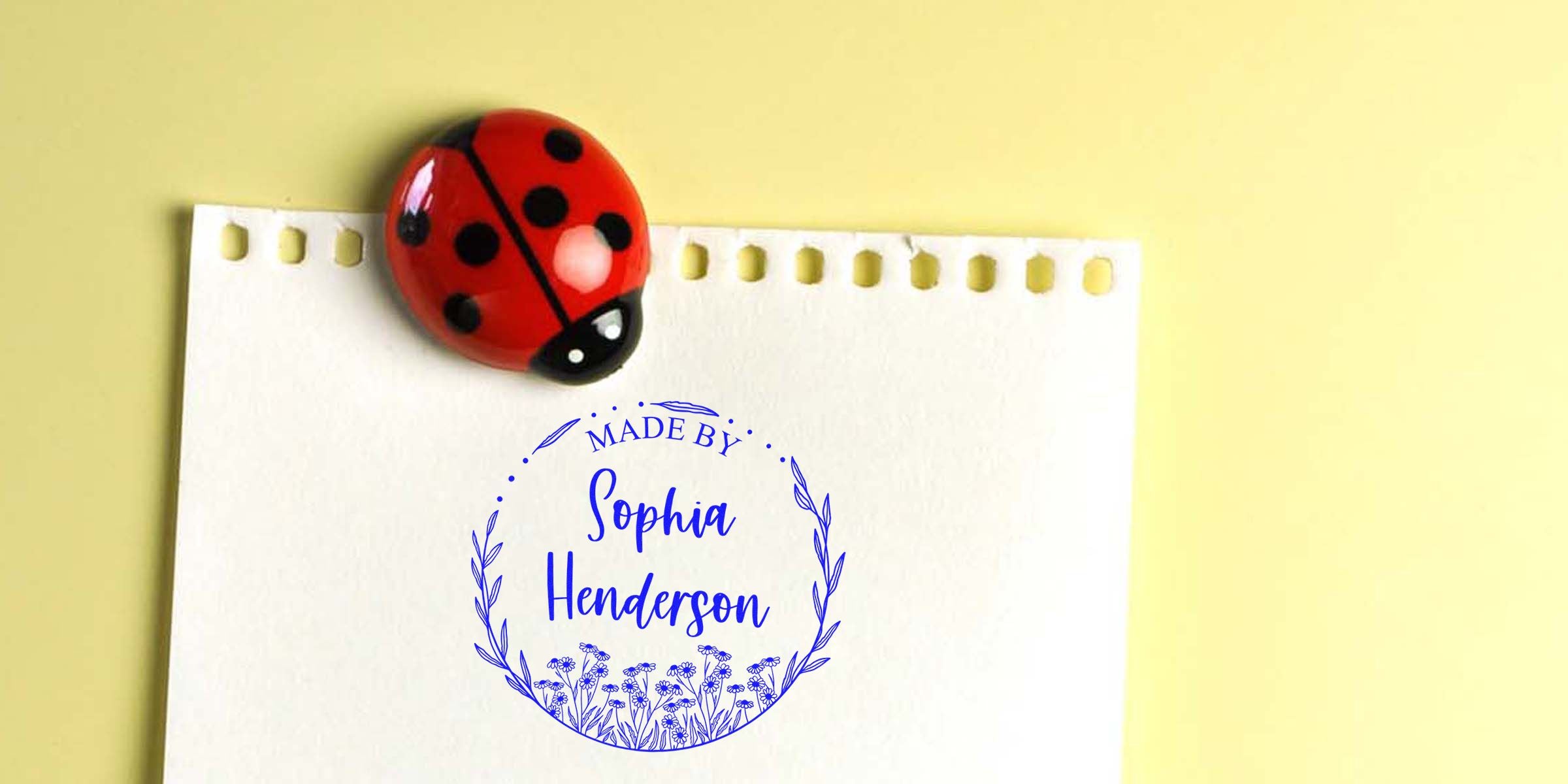 Red ladybug resting on a white card with a blue “Made by Sophia Henderson” stamp and laurel border.