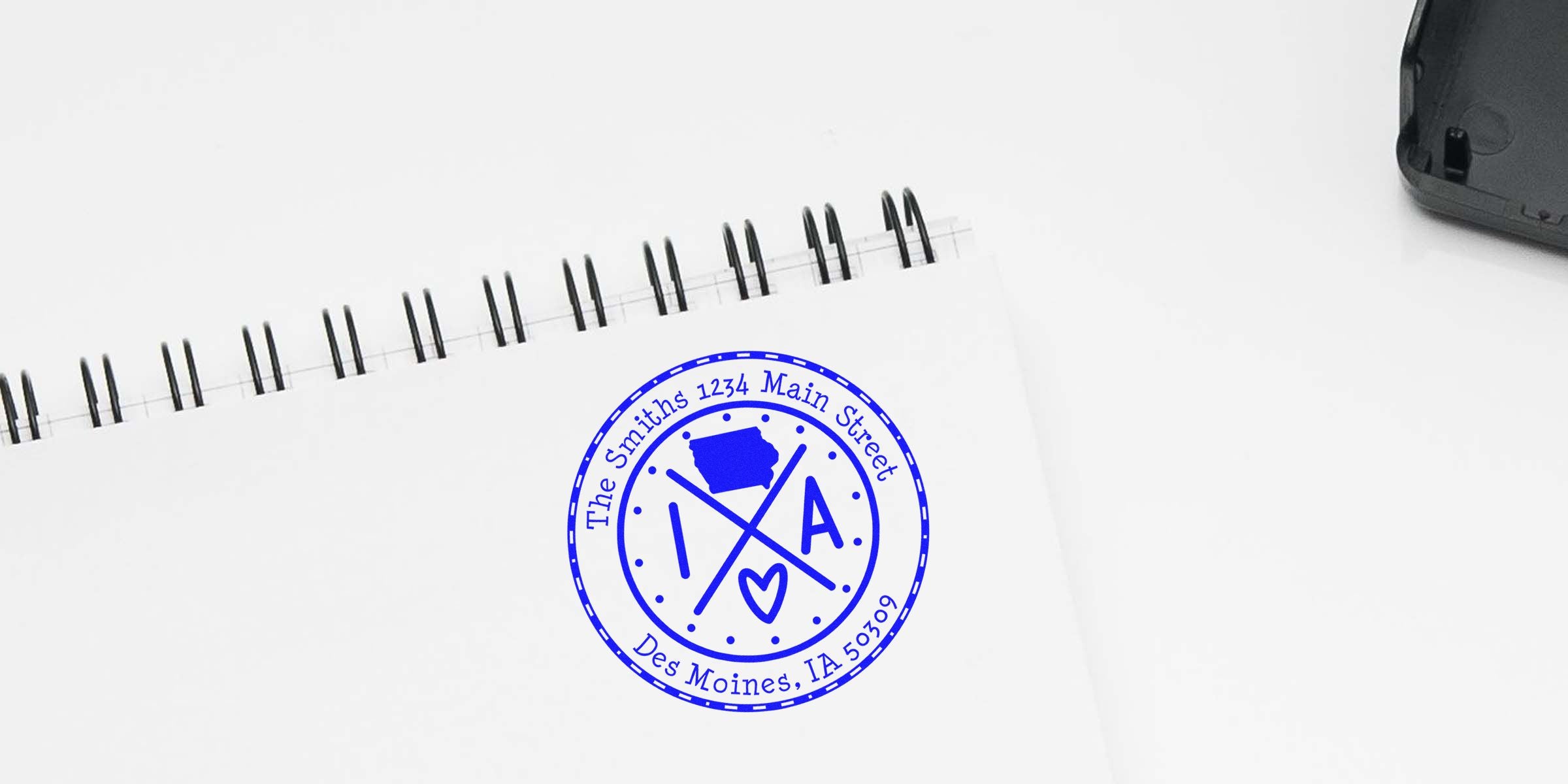 Blue circular stamp with the text "The Smiths 1234 Main Street Des Moines, IA 50309" on a white notebook.