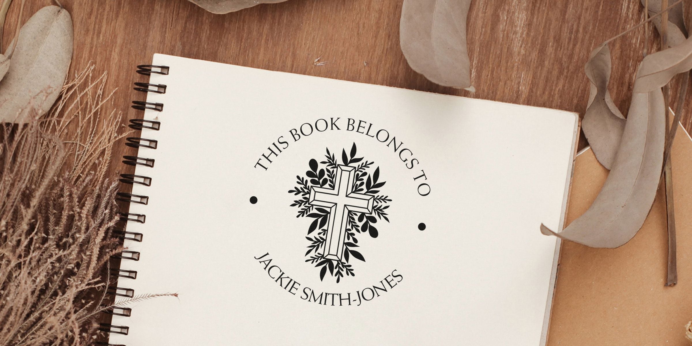 Circular emblem of a cross with leaves, surrounded by the text “This book belongs to Jackie Smith-Jones” on a white notebook.