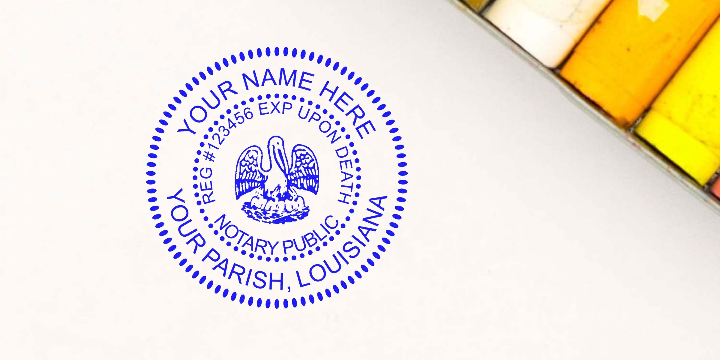 Blue circular notary stamp with pelican emblem and placeholder text "YOUR NAME HERE, YOUR PARISH, LOUISIANA" printed on white paper, angled near a set of yellow and orange pastel chalks — notary seal, legal stamp, Louisiana emblem.