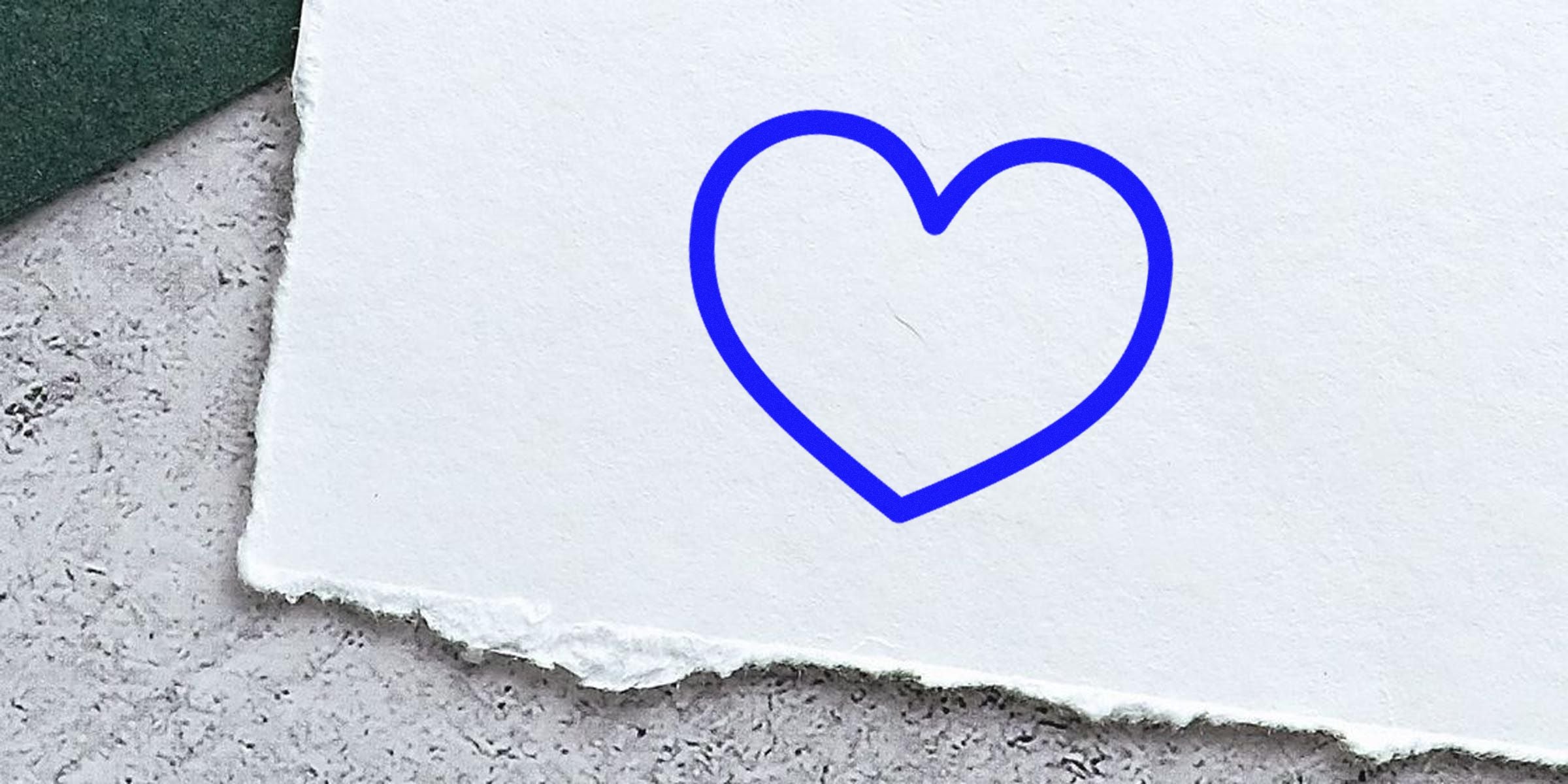 Blue outline heart drawn on a white textured surface/piece of paper.