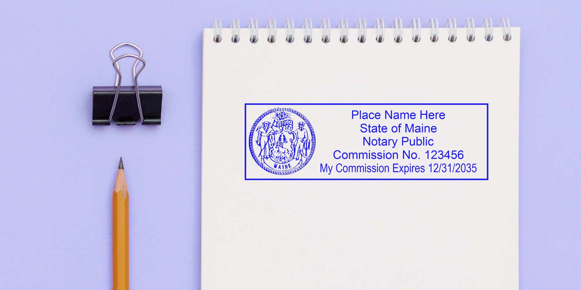 Top view spiral notebook page with blue State of Maine notary public stamp, sharpened pencil and black binder clip on lavender background