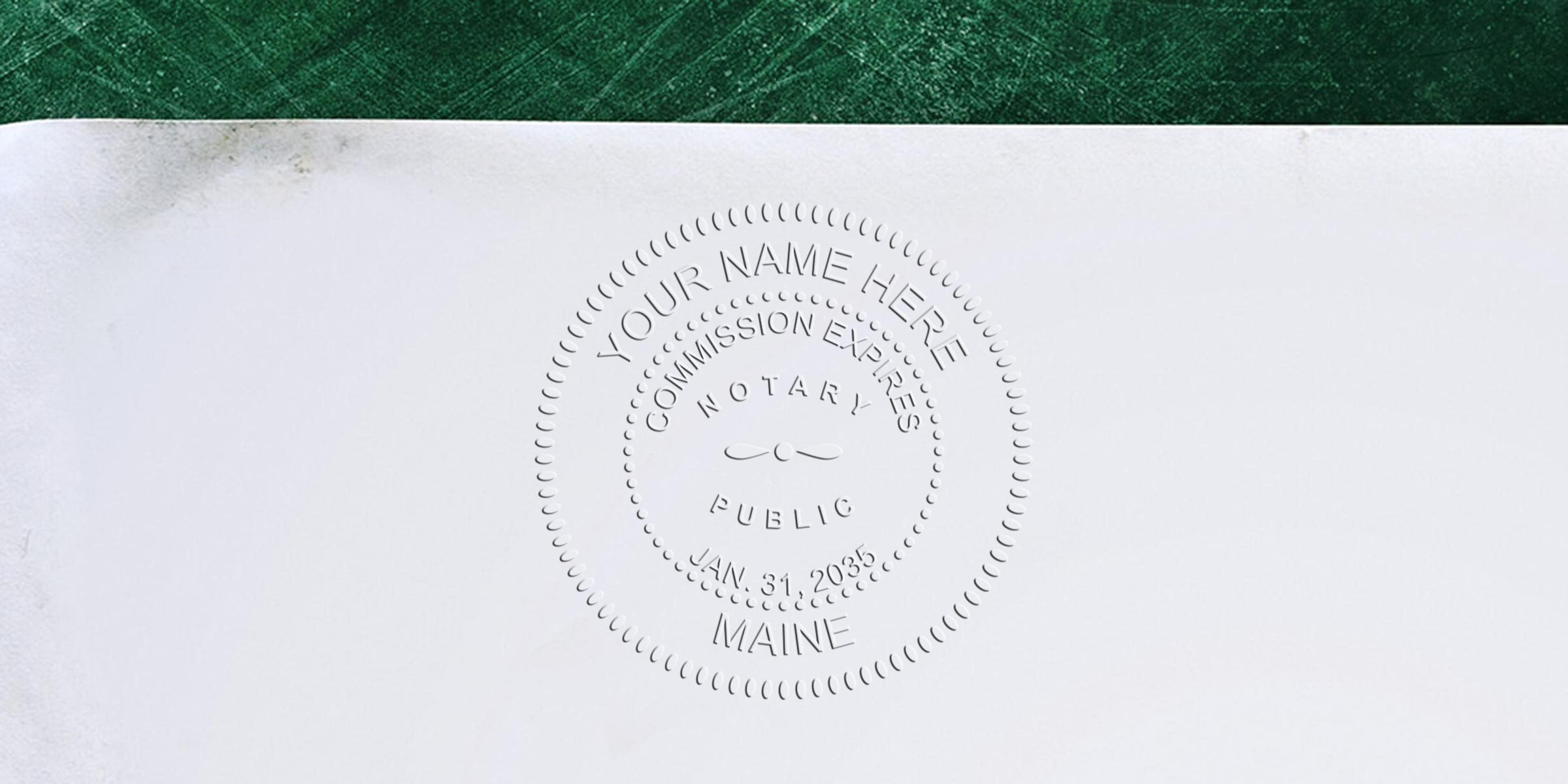 Embossed circular notary public seal on white paper showing placeholder text "Your Name Here," commission expires date, "Notary Public" and "Maine," with a textured green strip along the top edge