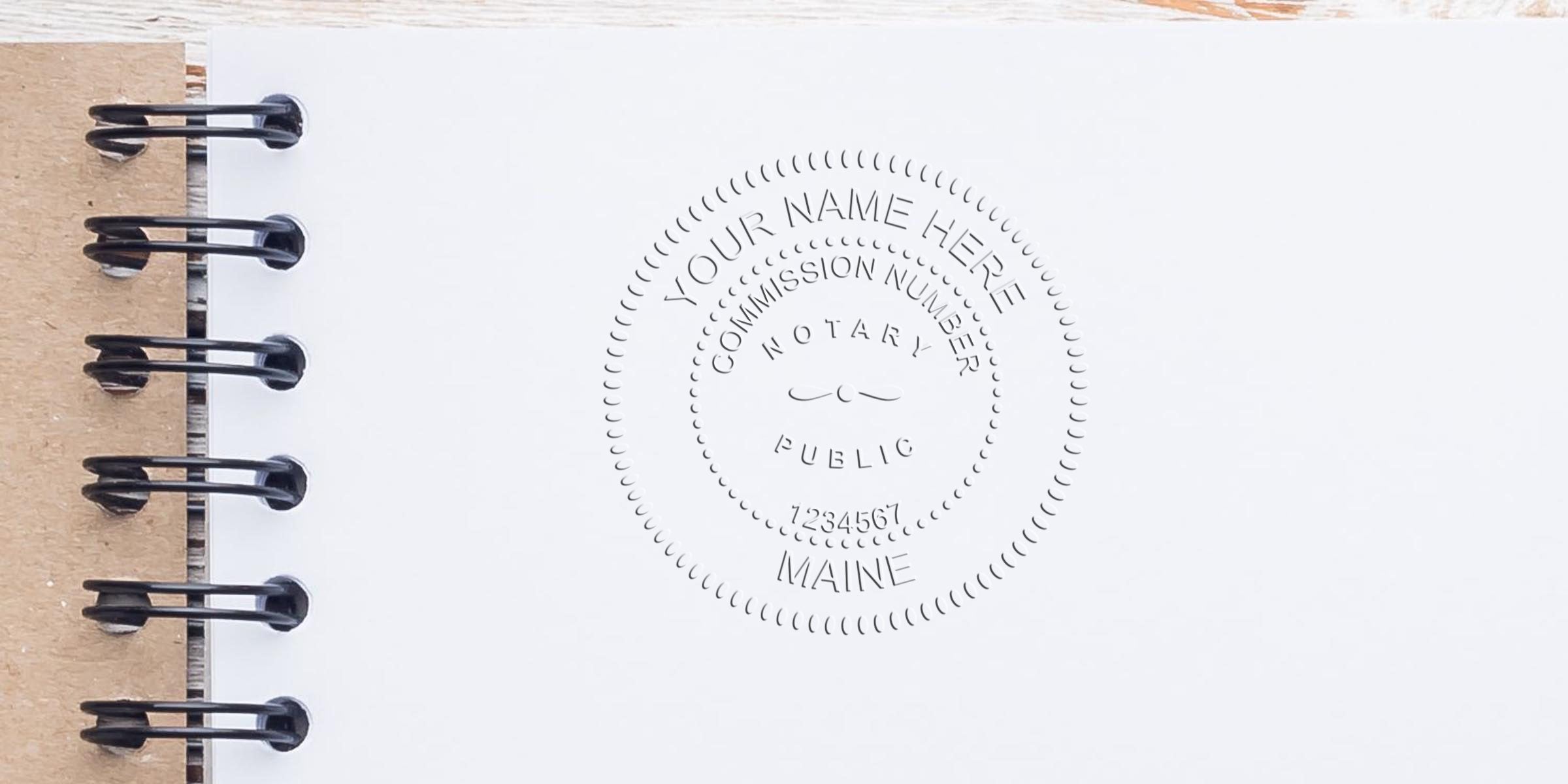 Spiral-bound notebook page with an embossed circular notary public seal reading "Your Name Here," commission number and "Maine" visible, close-up on white paper.