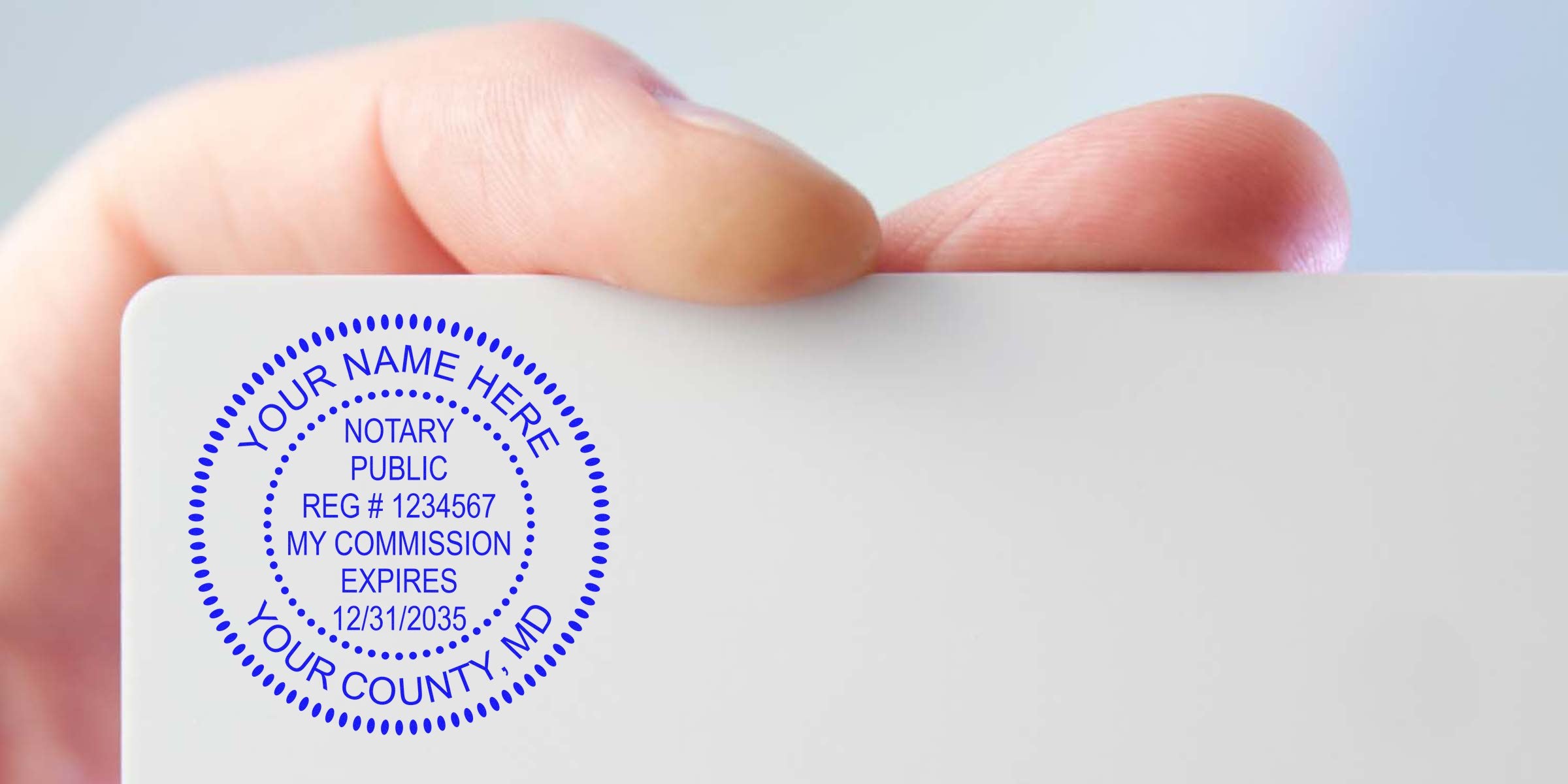 Close-up of a hand holding a white card stamped with a blue circular notary public seal showing placeholder name, registration number, commission expiration date and county text.