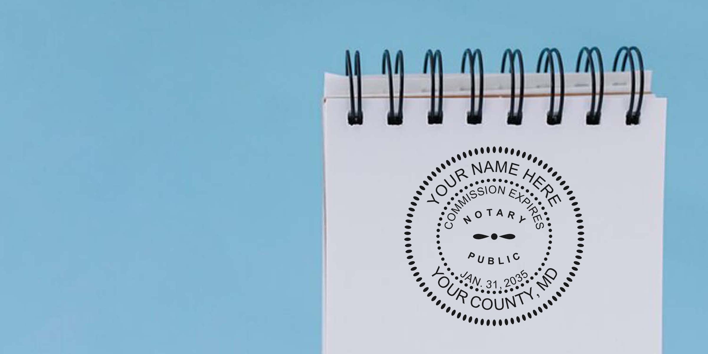 Spiral-bound white notepad on light blue background featuring a round black notary public stamp design with placeholder text "Your Name Here," "Commission Expires," county and date details.