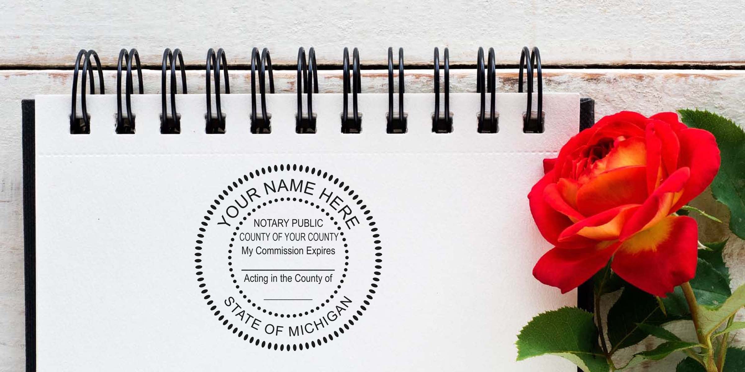Spiral notebook page stamped with a circular "Notary Public - State of Michigan" seal beside a vibrant red-yellow rose on a white wood background