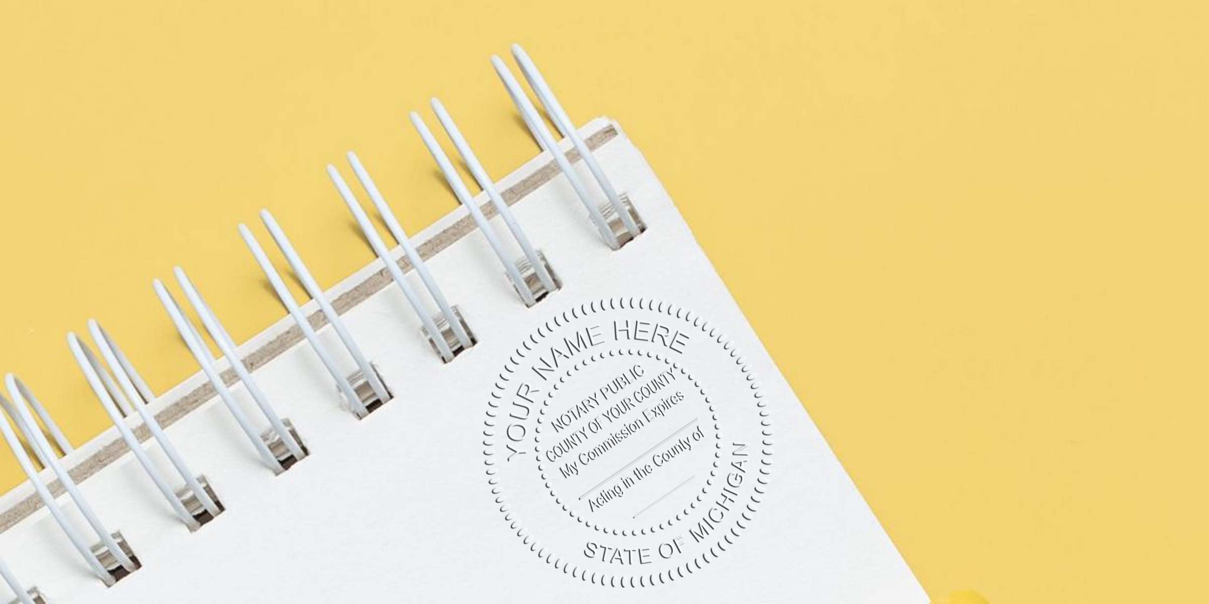 Close-up of white spiral-bound notebook corner with embossed circular notary seal reading "Your Name Here" on a yellow background