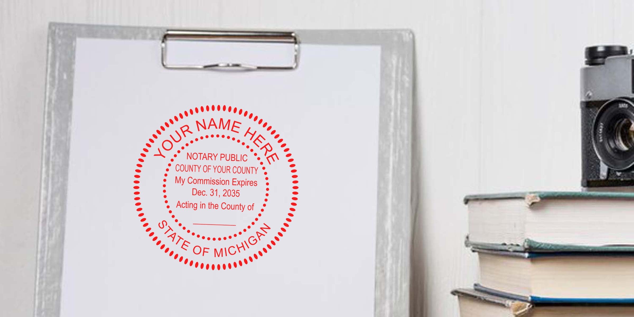 Clipboard with white paper showing a red circular Michigan notary stamp mockup, next to stacked books and a vintage camera on a light office desk — notary seal, paperwork, office decor
