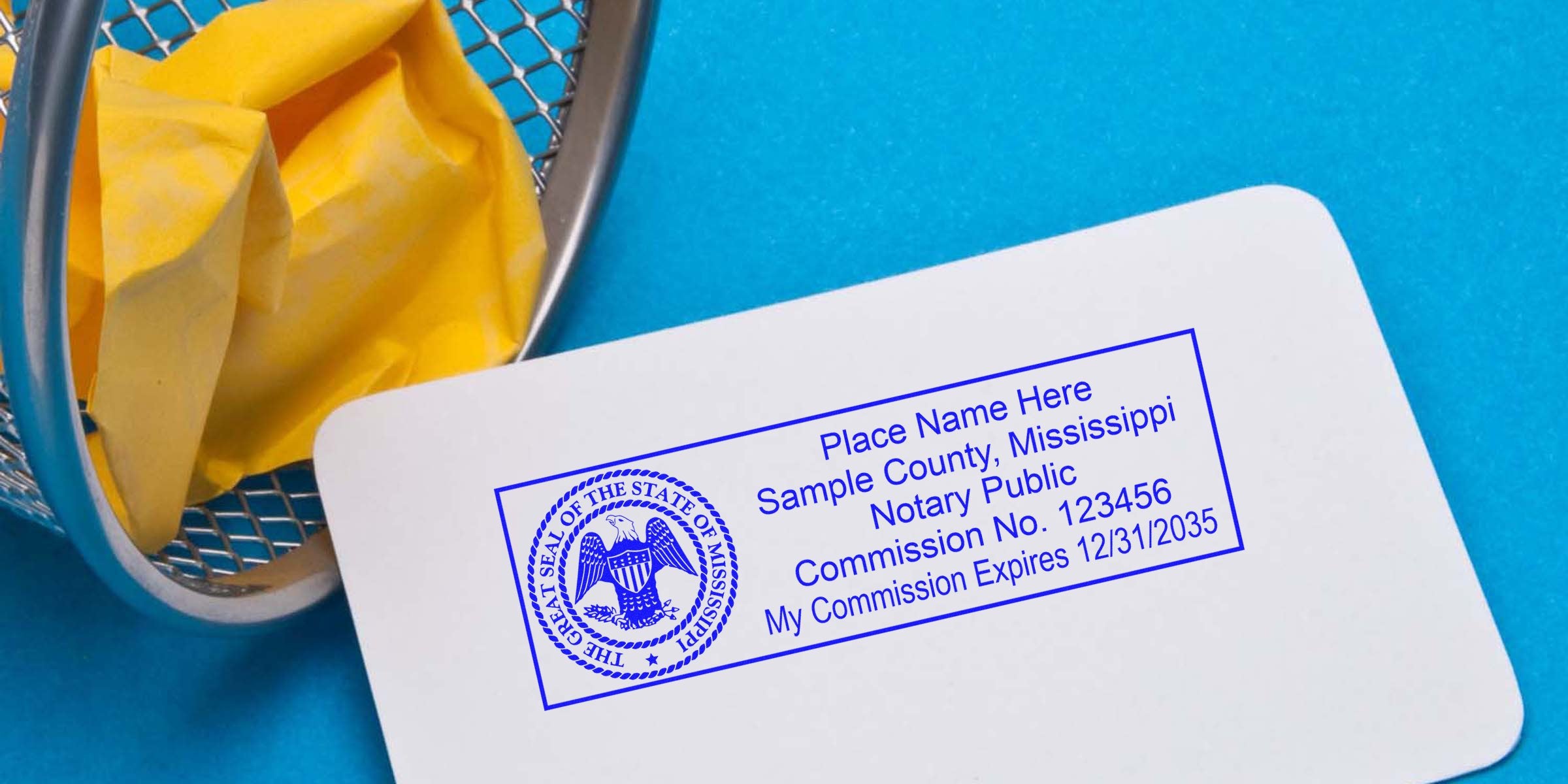 White card with blue Mississippi notary stamp sample and seal showing sample commission number, placed on bright blue background next to a metal trash bin holding crumpled yellow paper