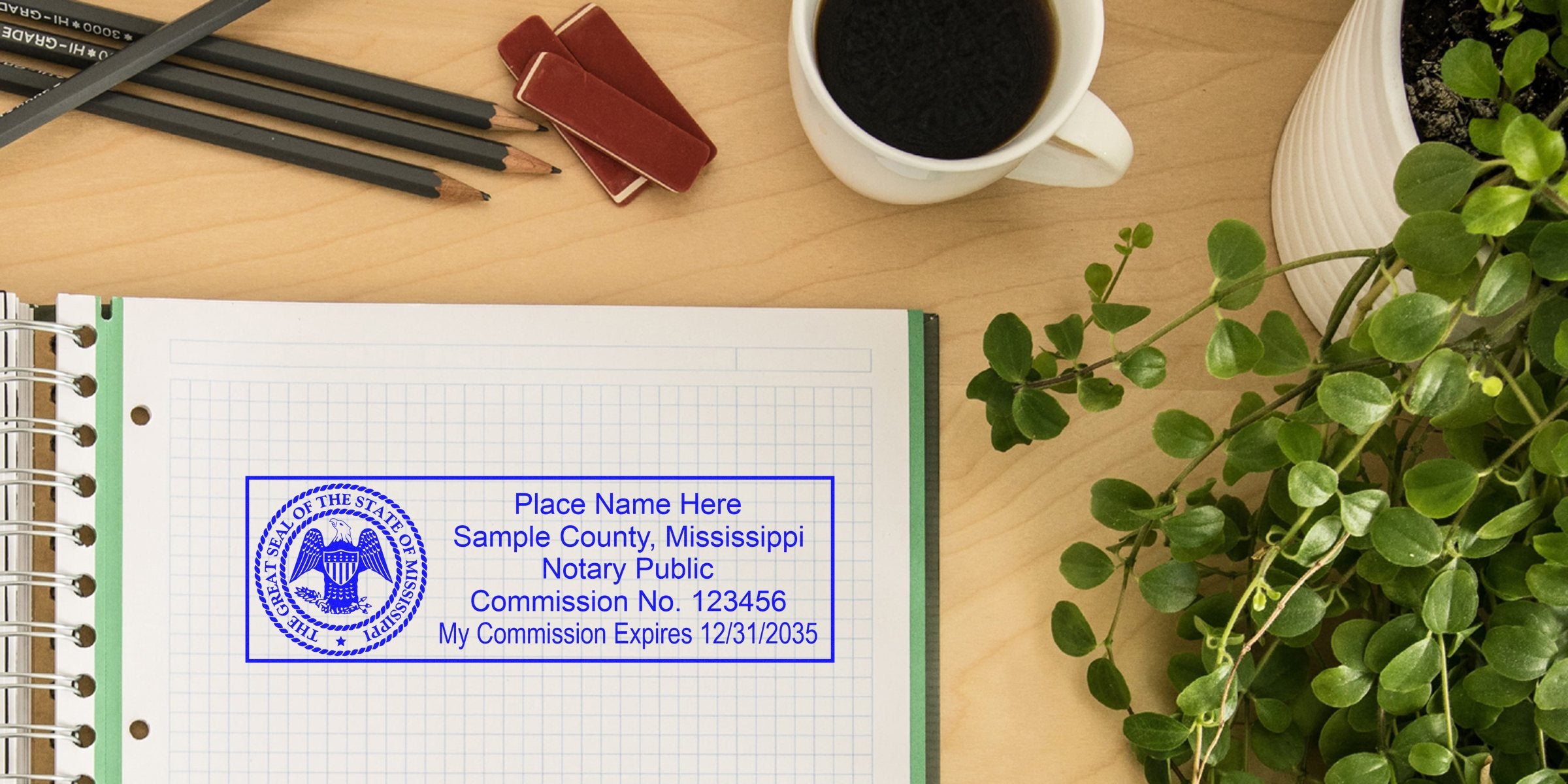 Top-down view of a wooden desk with spiral graph paper notebook stamped with a blue Mississippi notary sample seal and commission details, pencils, coffee cup, and green potted plant.
