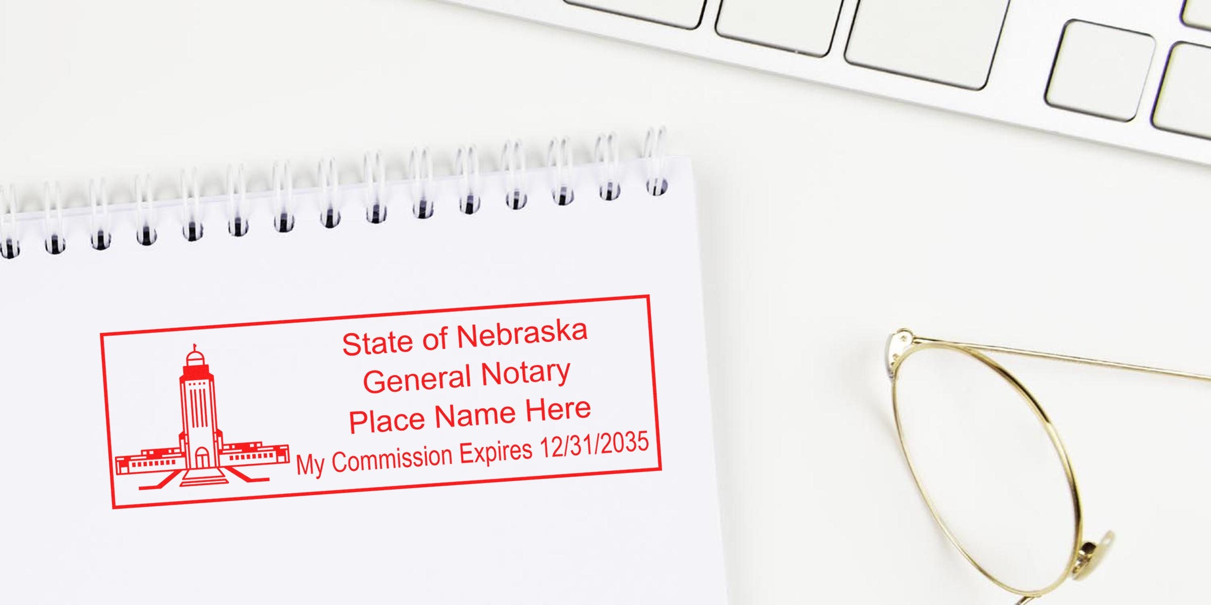 Top-down view of spiral notebook with a red "State of Nebraska General Notary" stamp showing commission expiry date, next to a keyboard and gold-rimmed glasses