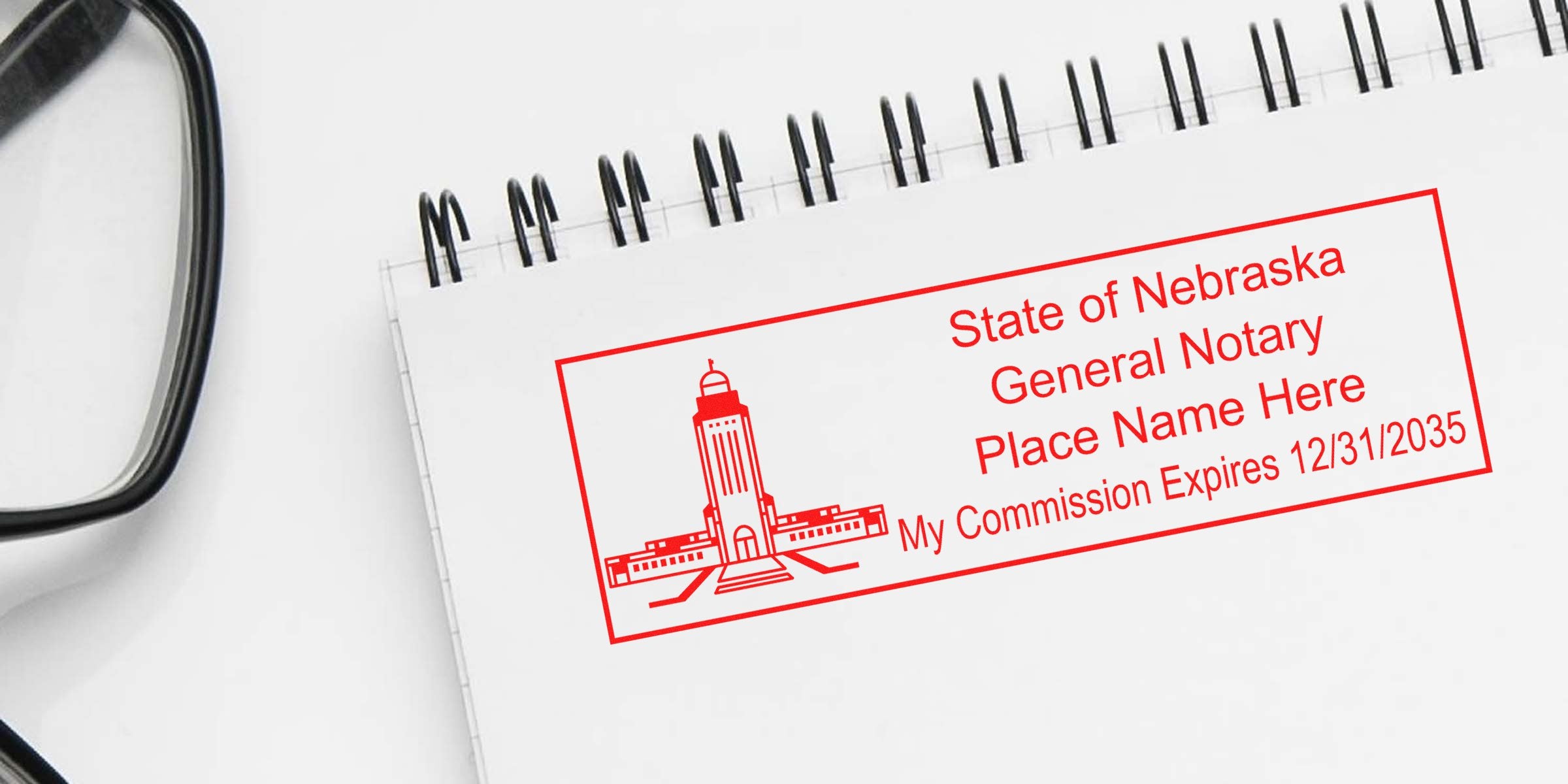 Red Nebraska notary stamp on a spiral notebook beside eyeglasses, featuring a capitol building graphic and text reading "State of Nebraska General Notary," placeholder name and commission expiration date.