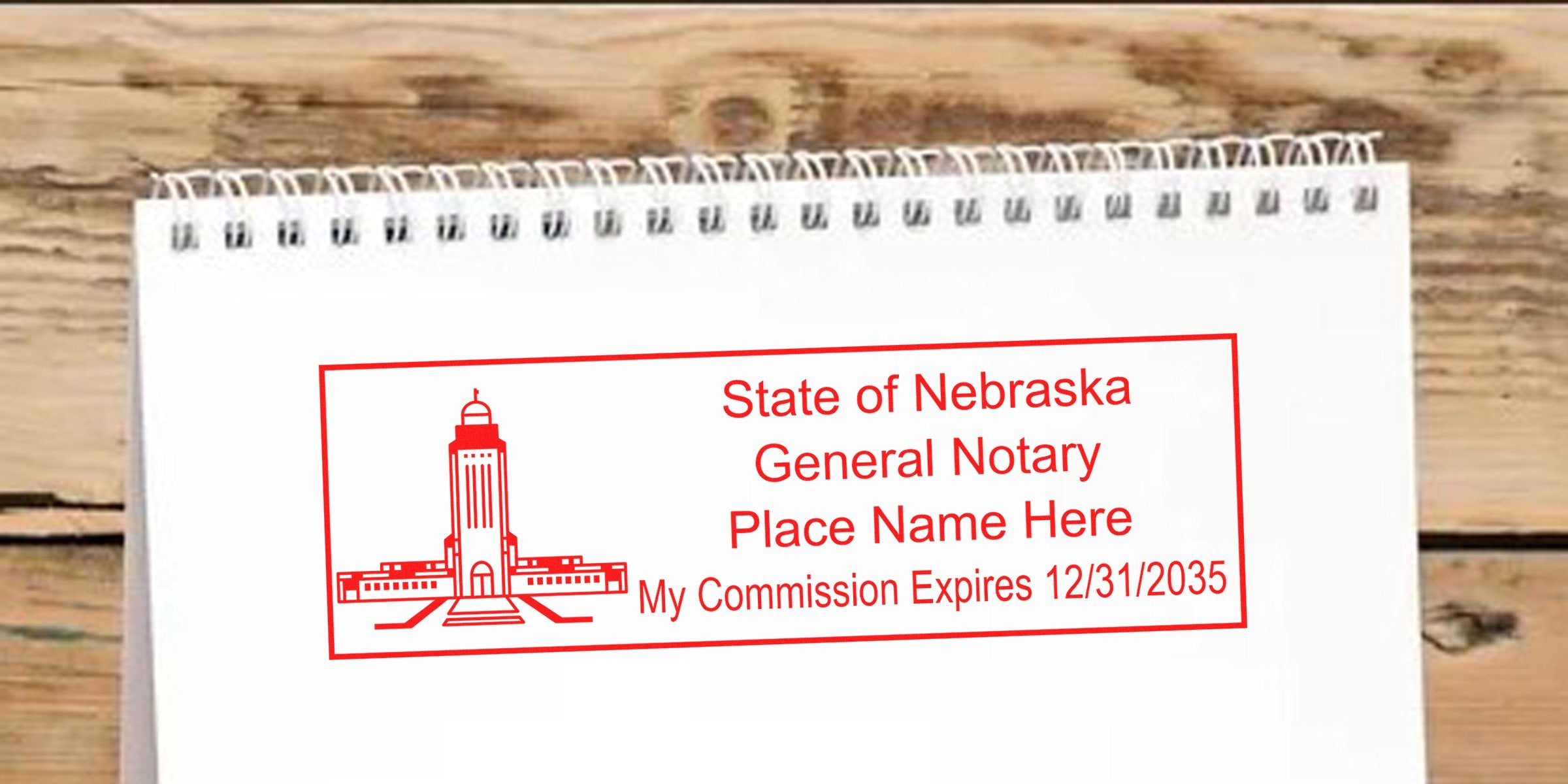 Red rectangular "State of Nebraska General Notary" stamp on white spiral notebook with Capitol tower illustration, placeholder "Place Name Here" and commission expiration date 12/31/2035.