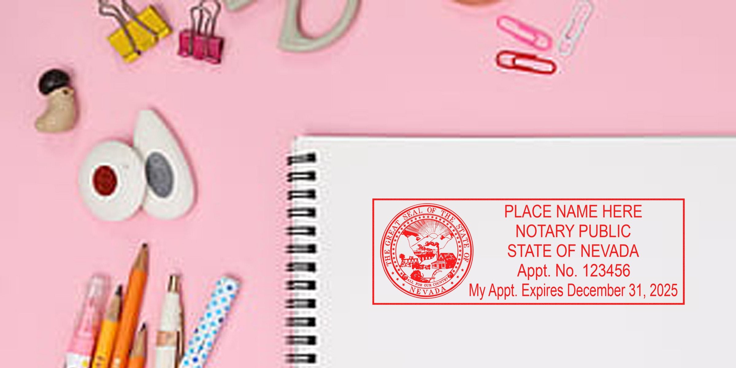 Top-view pink workspace with a spiral notebook showing a red Nevada notary public stamp, surrounded by pencils, pens, binder clips, paper clips and decorative washi tape.